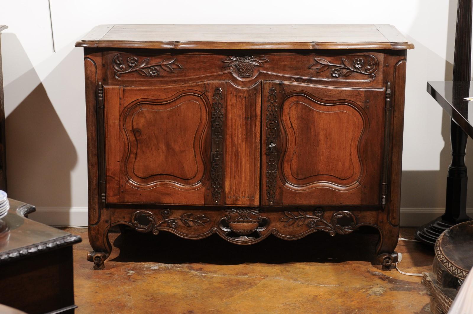 A French Louis XV style hand-carved walnut buffet from the early 19th century with floral décor, molded doors and pierced skirt. Born in the early years of the 19th century at a time when France was transitioning from the Consulat to Napoleon's