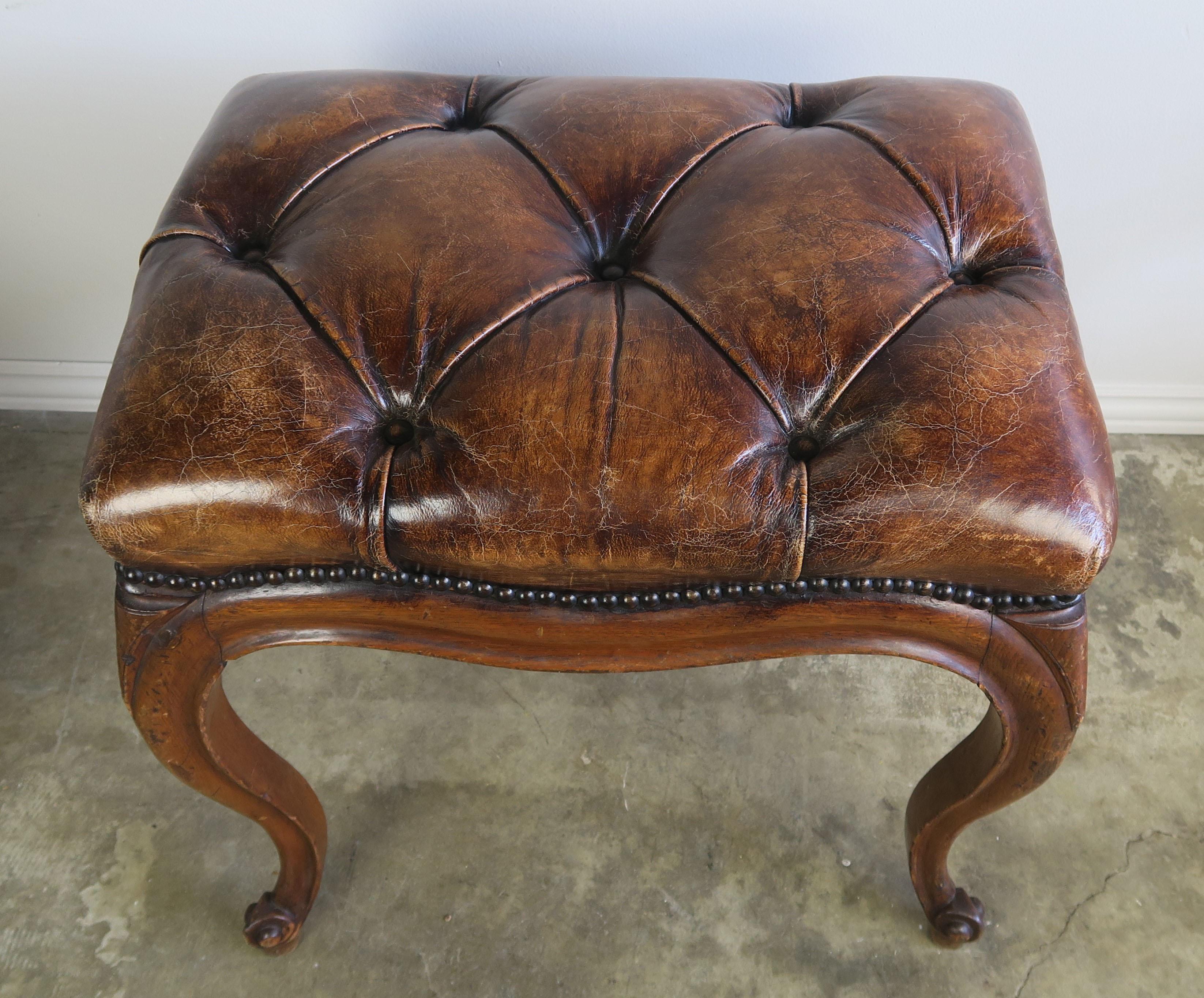 French Louis XV style leather tufted bench with nailhead trim detail. The walnut bench stands on four cabriole legs that end in ram's head feet. Beautiful worn leather in great condition.