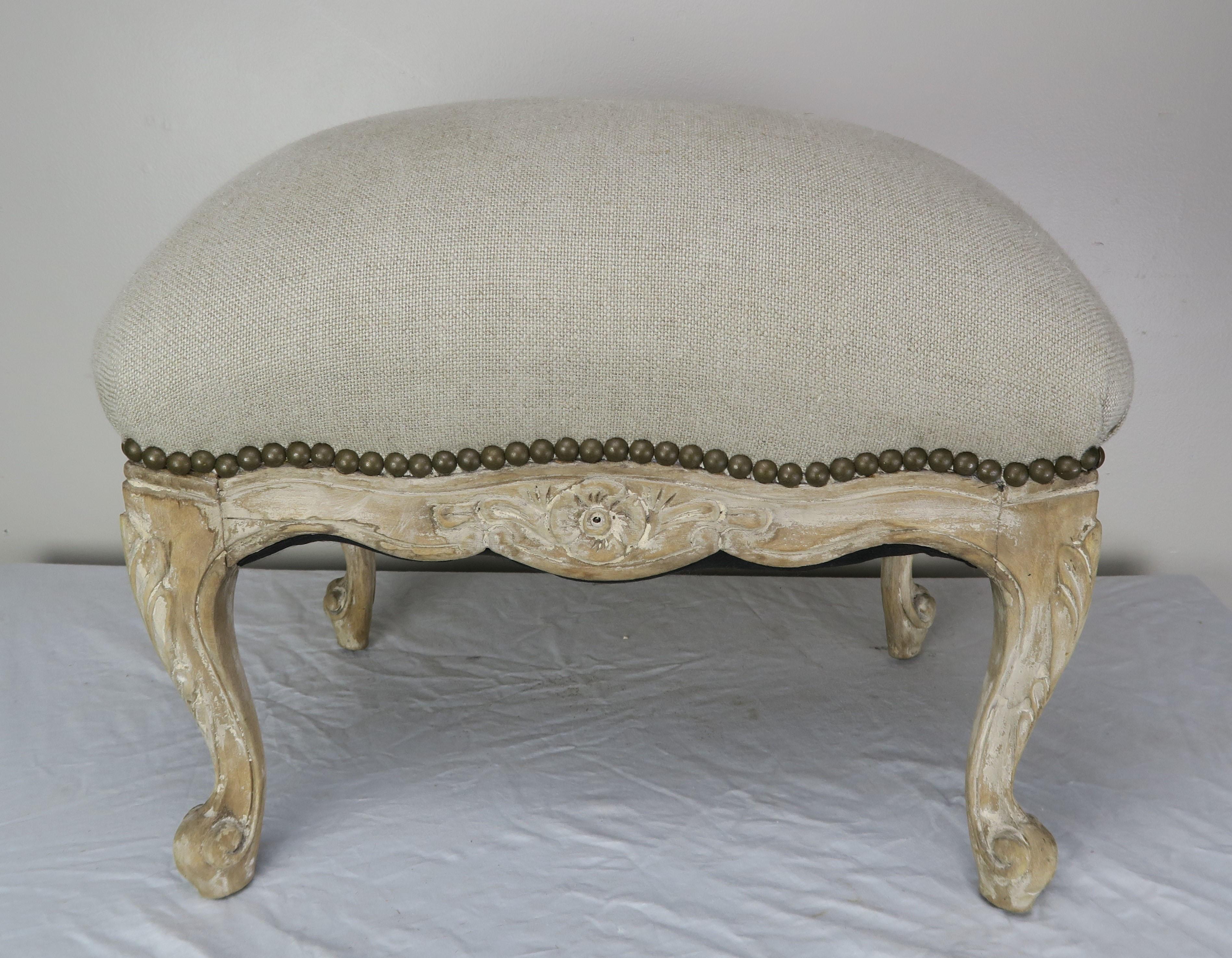 French Louis XV style bench upholstered in a neutral oatmeal colored Belgium washed linen. The accent bench is detailed with antique brass colored nail heads. The bench stands on four cabriole legs that end in rams head feet. Subtle but beautiful