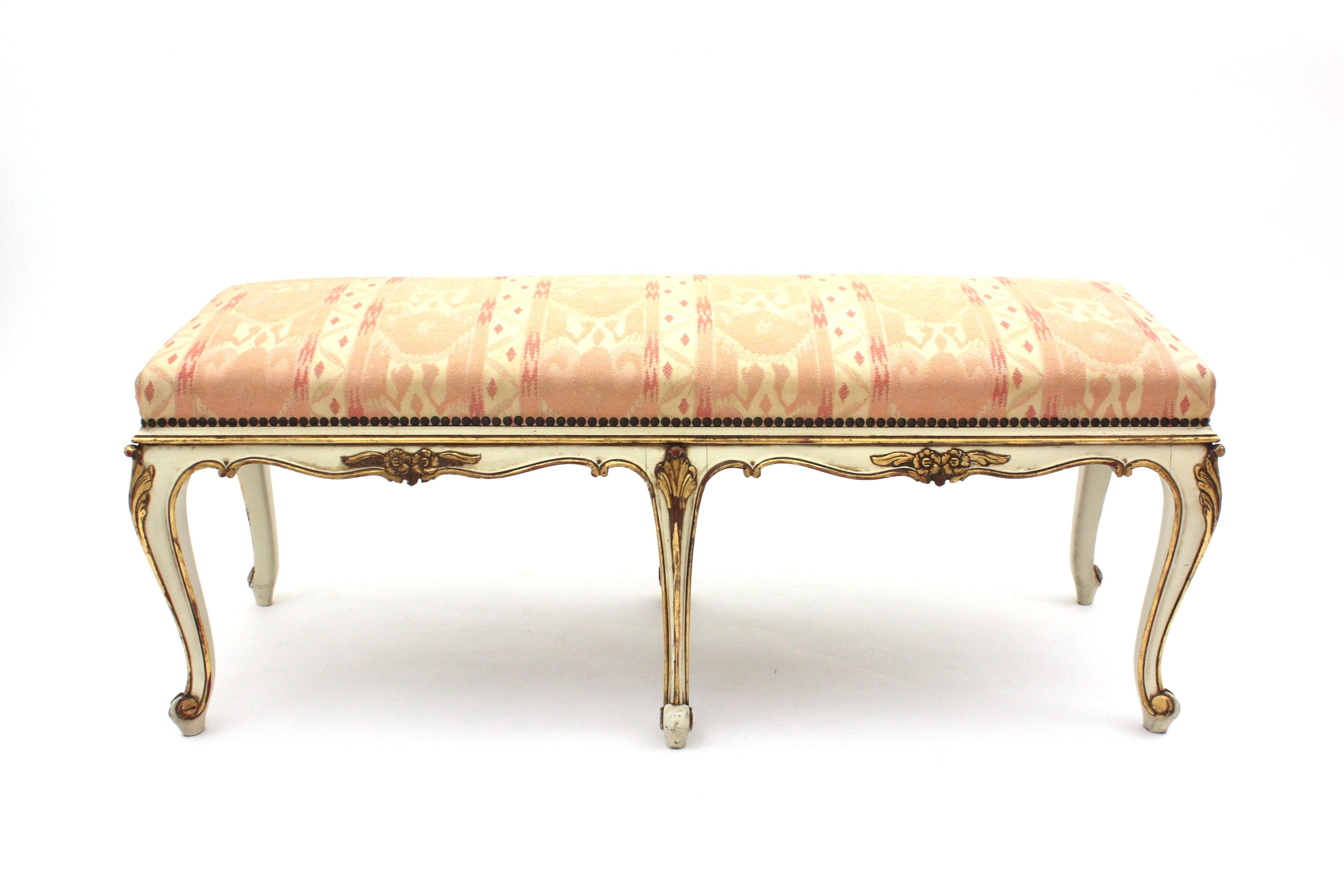 Louis XV style carved parcel-gilt wood bench patinated in ivory color, France, 1930s-1940s.
This bench or stool is raised on six cabriole shaped legs with carved floral knees and foliage motifs and it is accented by decorative gold gilt