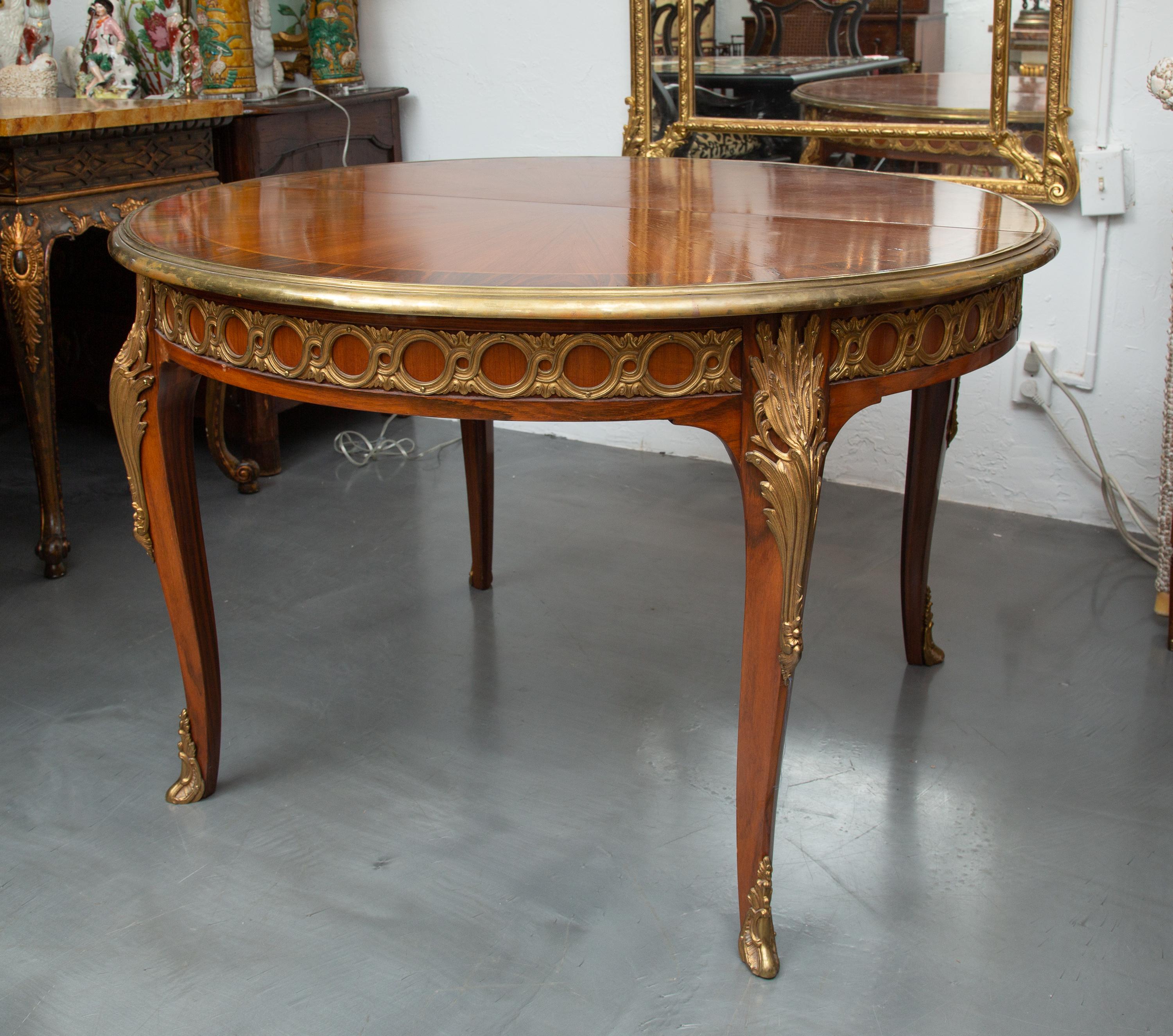 This is a lovely French Louis XV style dining table, the mahogany top banded with rosewood and brass-banded edge, above frieze with interlocking circle ornamentation, supported by four cabriole legs with gilt metal mounts on the knees and