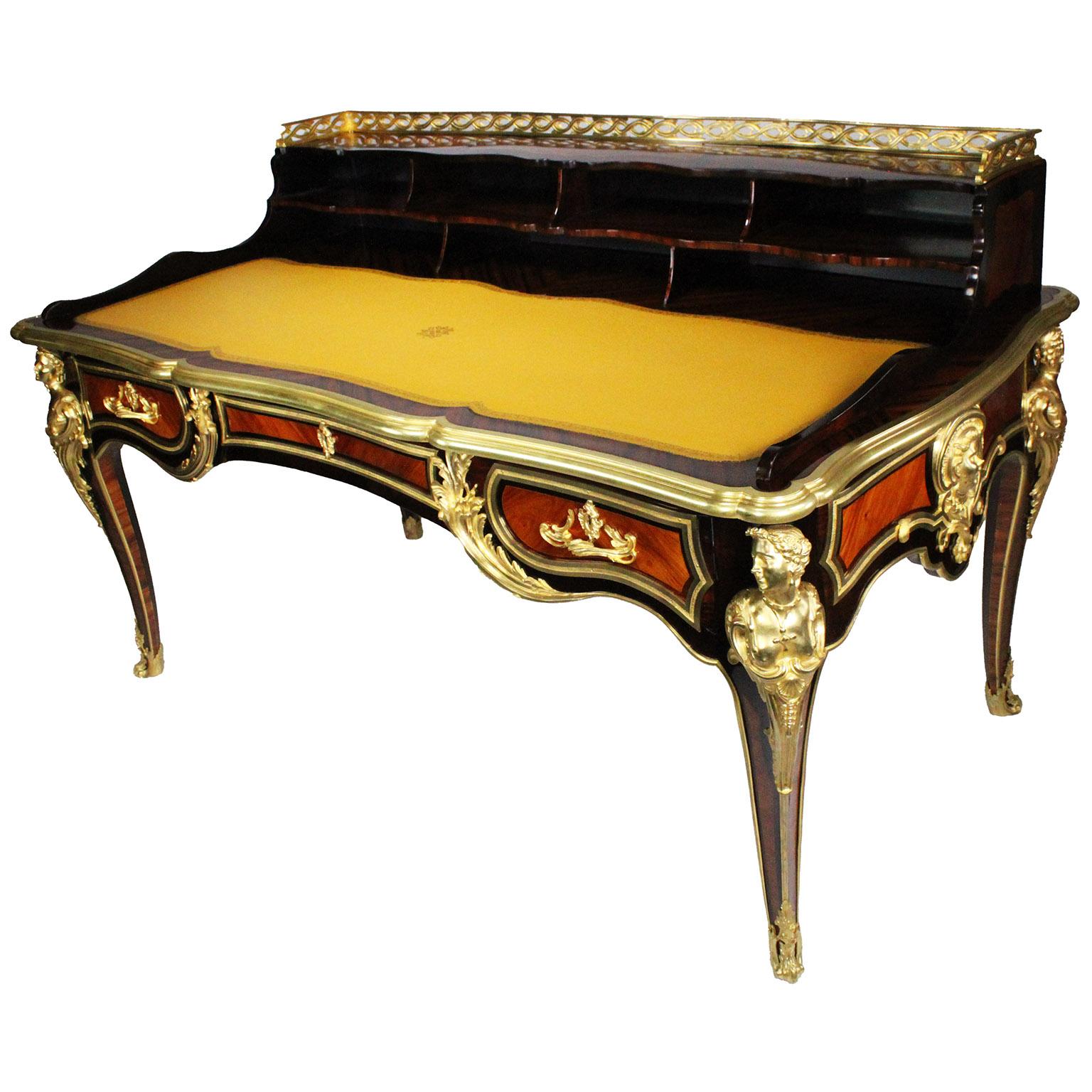 Raffinata scrivania francese in stile Luigi XV in mogano, palissandro e legno satinato con montatura in bronzo dorato. Il piano rettangolare sagomato è incastonato con un pannello di scrittura in pelle con lavorazione recente, sormontato da un