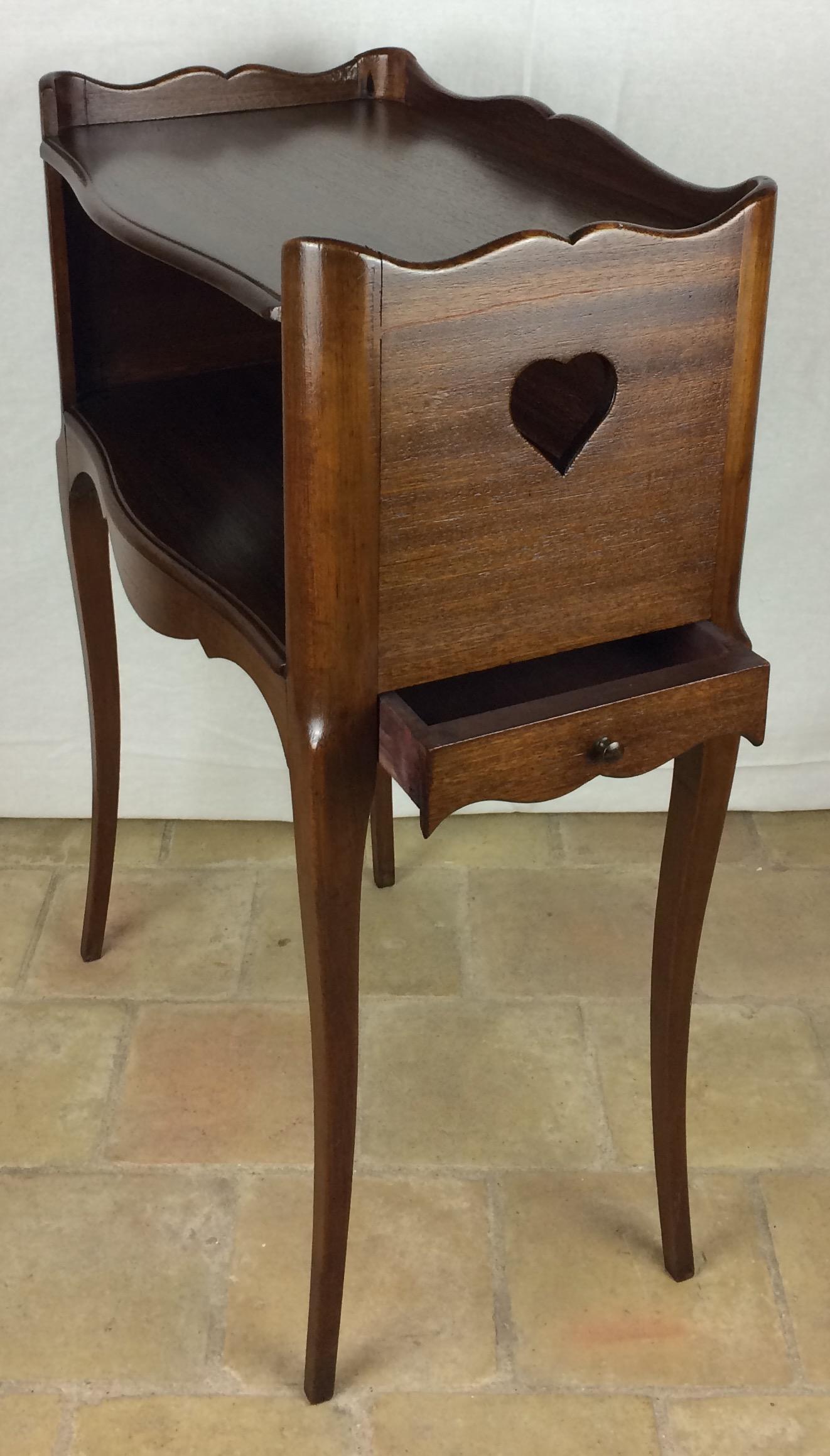 A Louis XV style country French side table or nightstand made of solid mahogany, with open niche and pierced cut-out heart shapes on the sides. Scalloped apron and gallery surrounding the top. One drawer. 

Very good quality table with curved