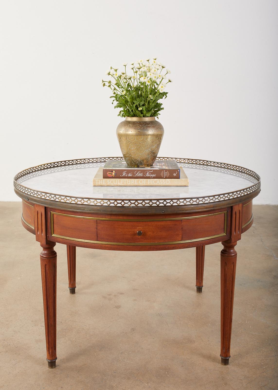 Stately French Bouillotte table or cocktail table made in the grand Louis XVI style. Features a white marble Carrara top and bronze mounts on the case. The circular marble top has a pierced brass galleried edge over a two-drawer bronze mounted