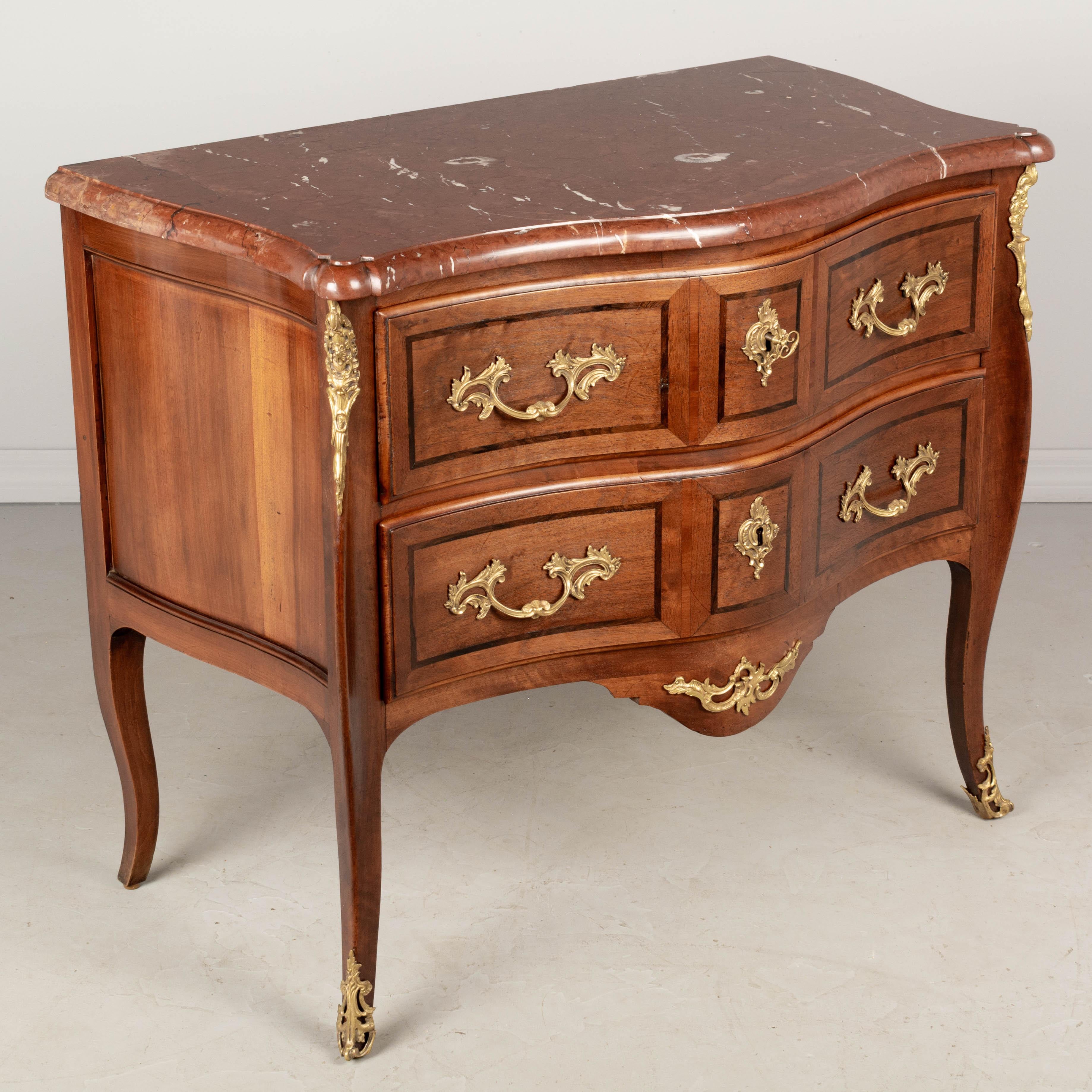 An early 20th century French Louis XV style bronze mounted marble top marquetry commode, finely crafted of solid walnut with rosewood inlay. Two dovetailed drawers with working locks and one key. Elegant serpentine form and slender cabriole legs.