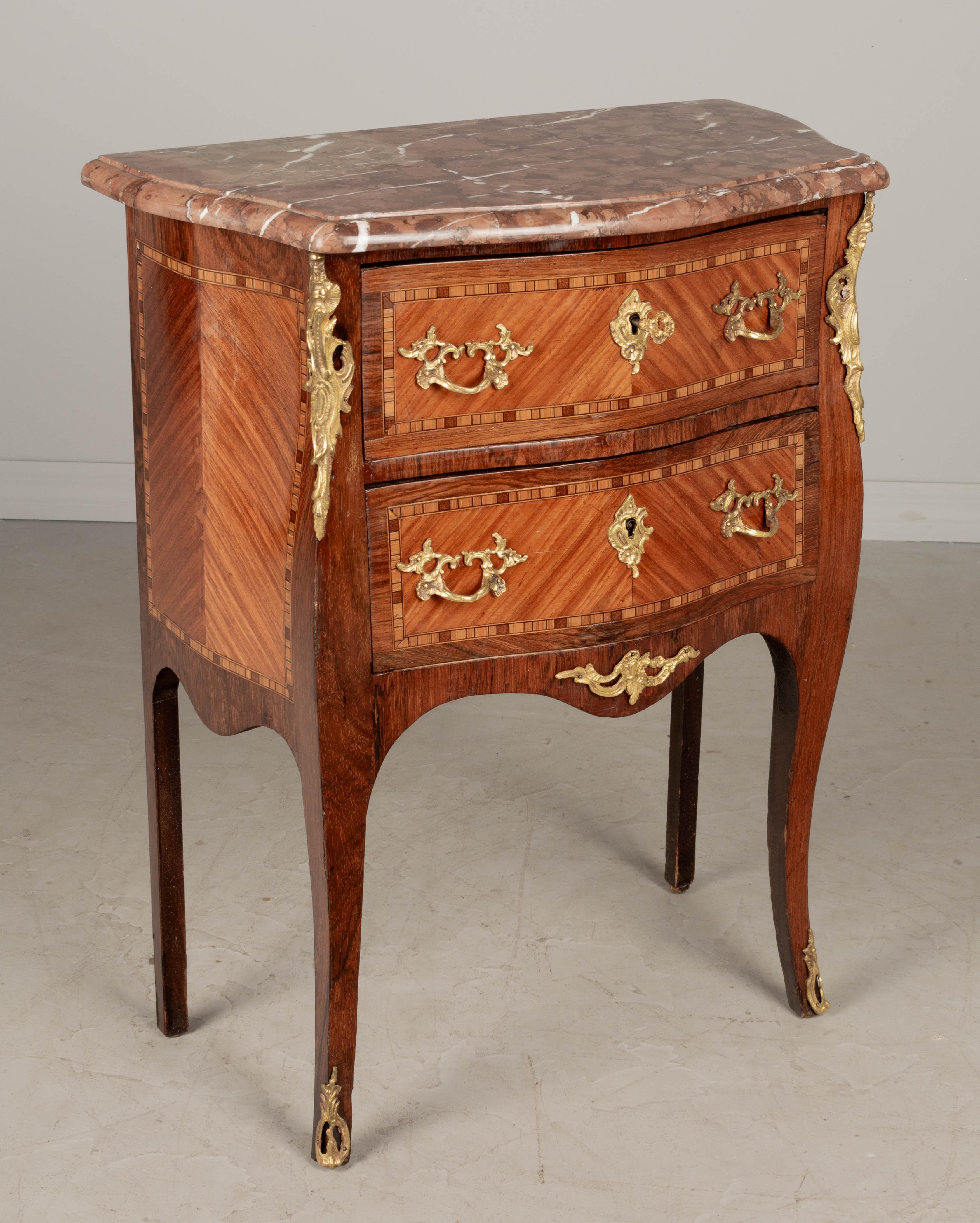 An early 20th century French Louis XV style bronze mounted marble top marquetry commode, finely crafted of solid mahogany with inlaid veneers of walnut, mahogany and various exotic woods. Elegant serpentine form and slender cabriole legs. French