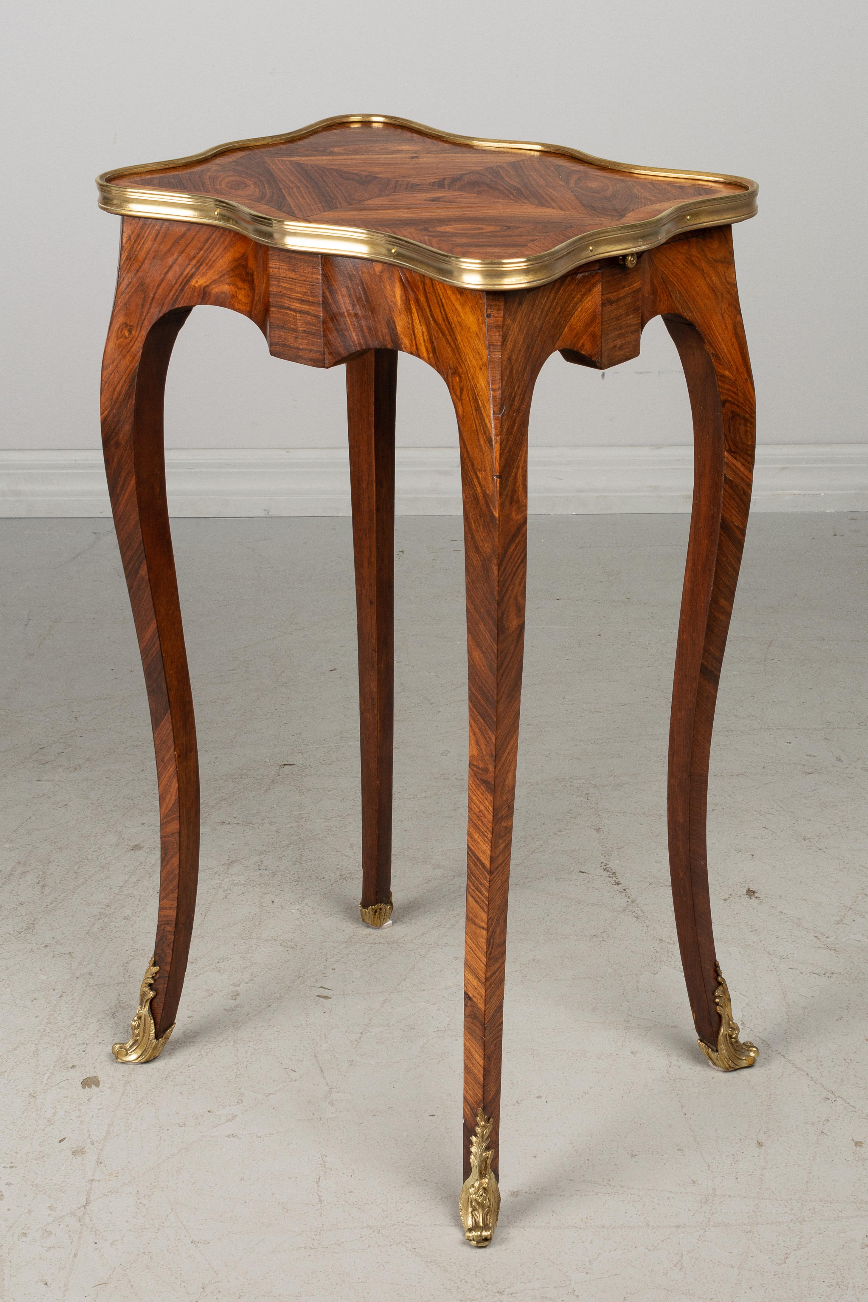 A fine Louis XV style French marquetry side table with inlaid veneer of bois de Violette rosewood. Hidden dovetailed drawer and a small pullout / pull-out tray with leather surface. Polished bronze trim surrounds the shaped tabletop. Slim curved