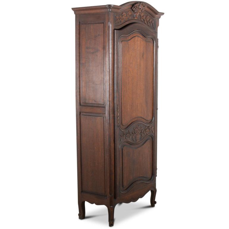A French, solid oak, Louis XV-style, single-door armoire or ‘bonnetiere’, the single door having two shaped raised panels within a serpentine shaped frame with central carved flowers. The crown of the piece is embellished with a carved oak floral