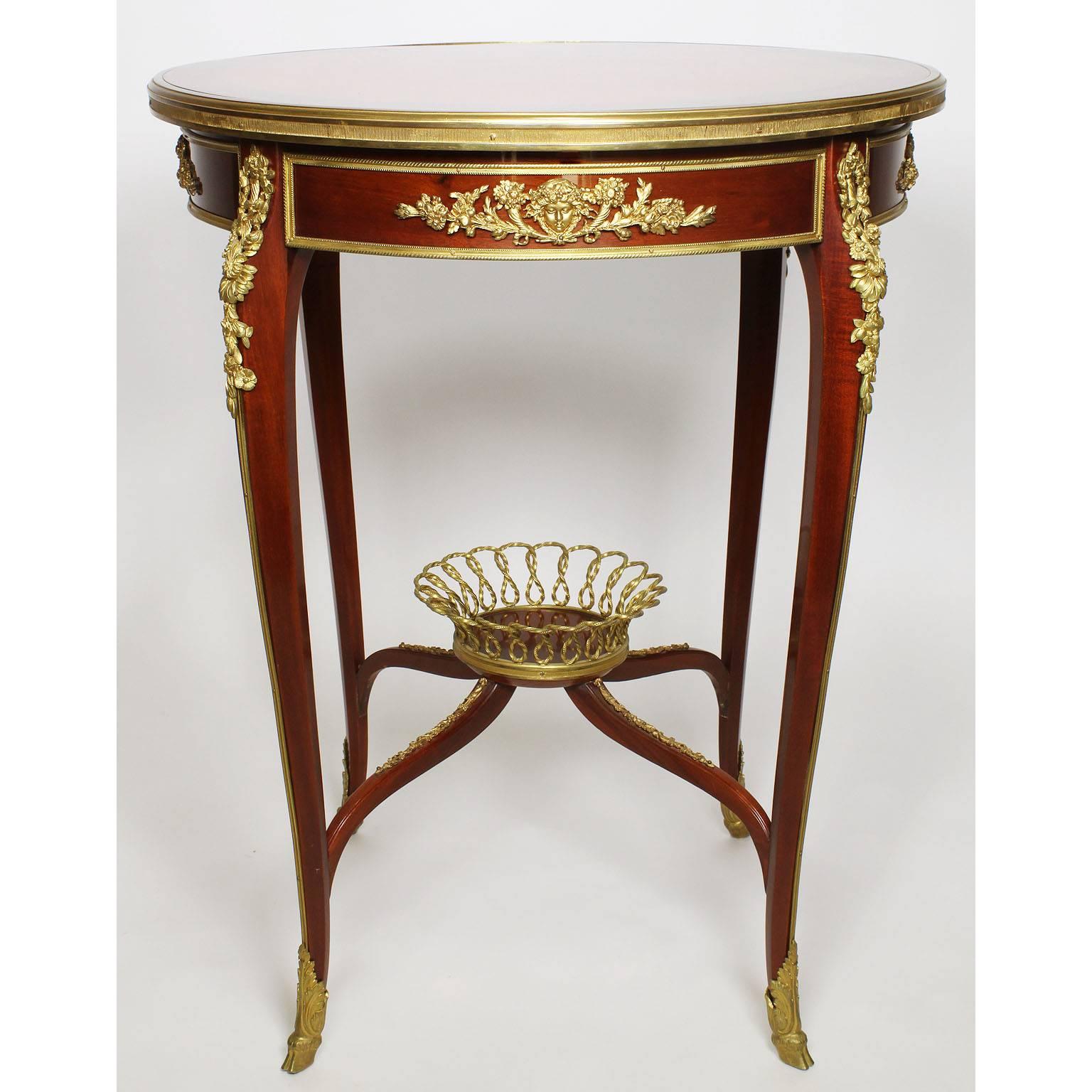 Table d'appoint de style Louis XV en acajou et marqueterie de bois de tulipier, montée sur bronze doré. Le plateau circulaire est incrusté d'une marqueterie de motifs floraux et d'une parqueterie symétrique. Le tablier est centré de montures en