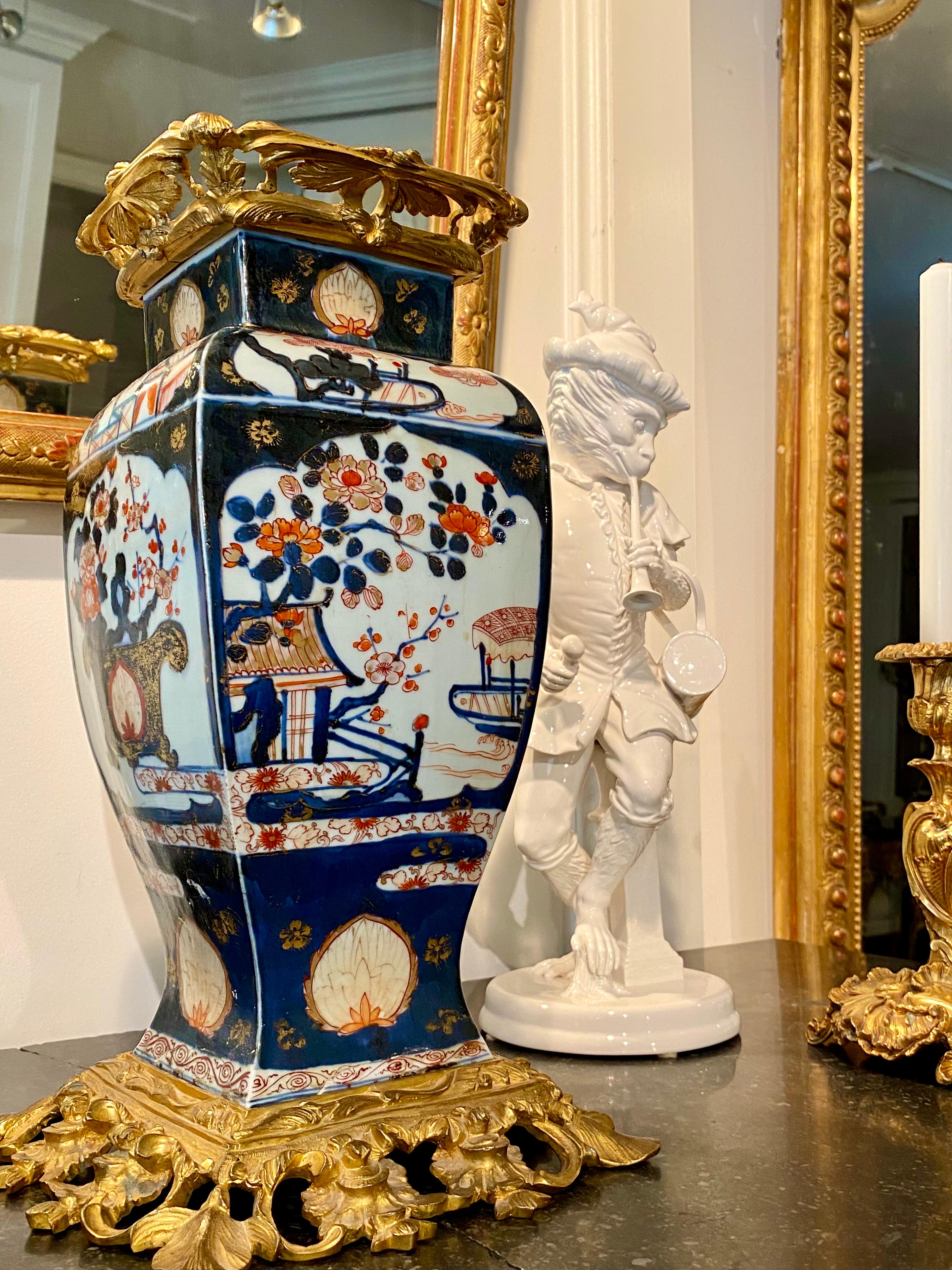 Of squared baluster form decorated with underglaze blue with red and gilt highlights and painted with boats in a harbor and flowers issuing from a vase with a foliate-cast gilt bronze pierced rim and spreading foot. Very beautiful vase, lovely