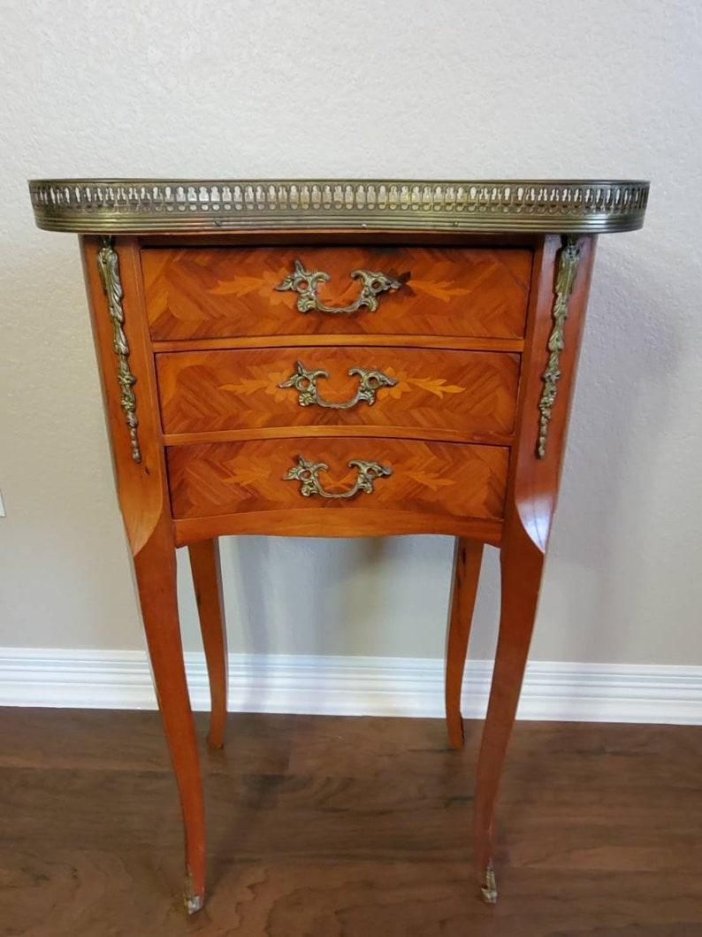 An elegant vintage Louis XV style, uniquely shaped kidney-form side table / bedside cabinet. Handcrafted in the second quarter of the 20th century, having a pierced gilt-metal gallery surrounding top with floral marquetry, three dovetailed drawers,
