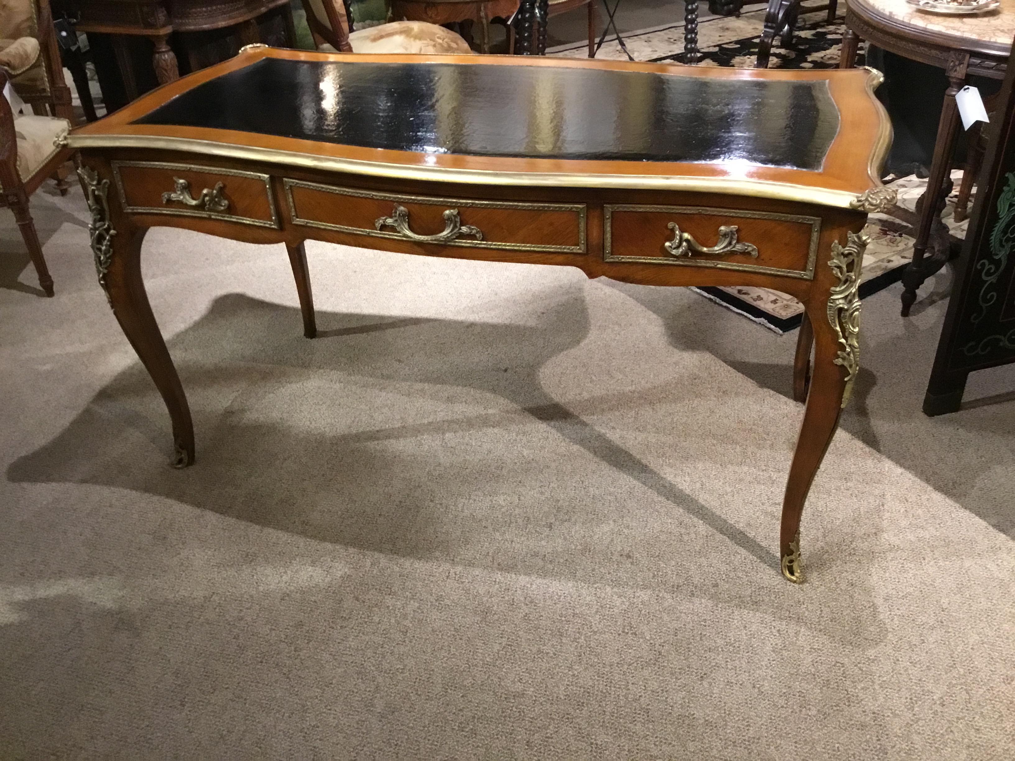 Mid-20th century, the serpentine top with bronze edge moldings and decorative corners, and
An inset tooled leather top, the front fitted with three side by side drawers, raised o cabriole
Legs with ormolu mounts.