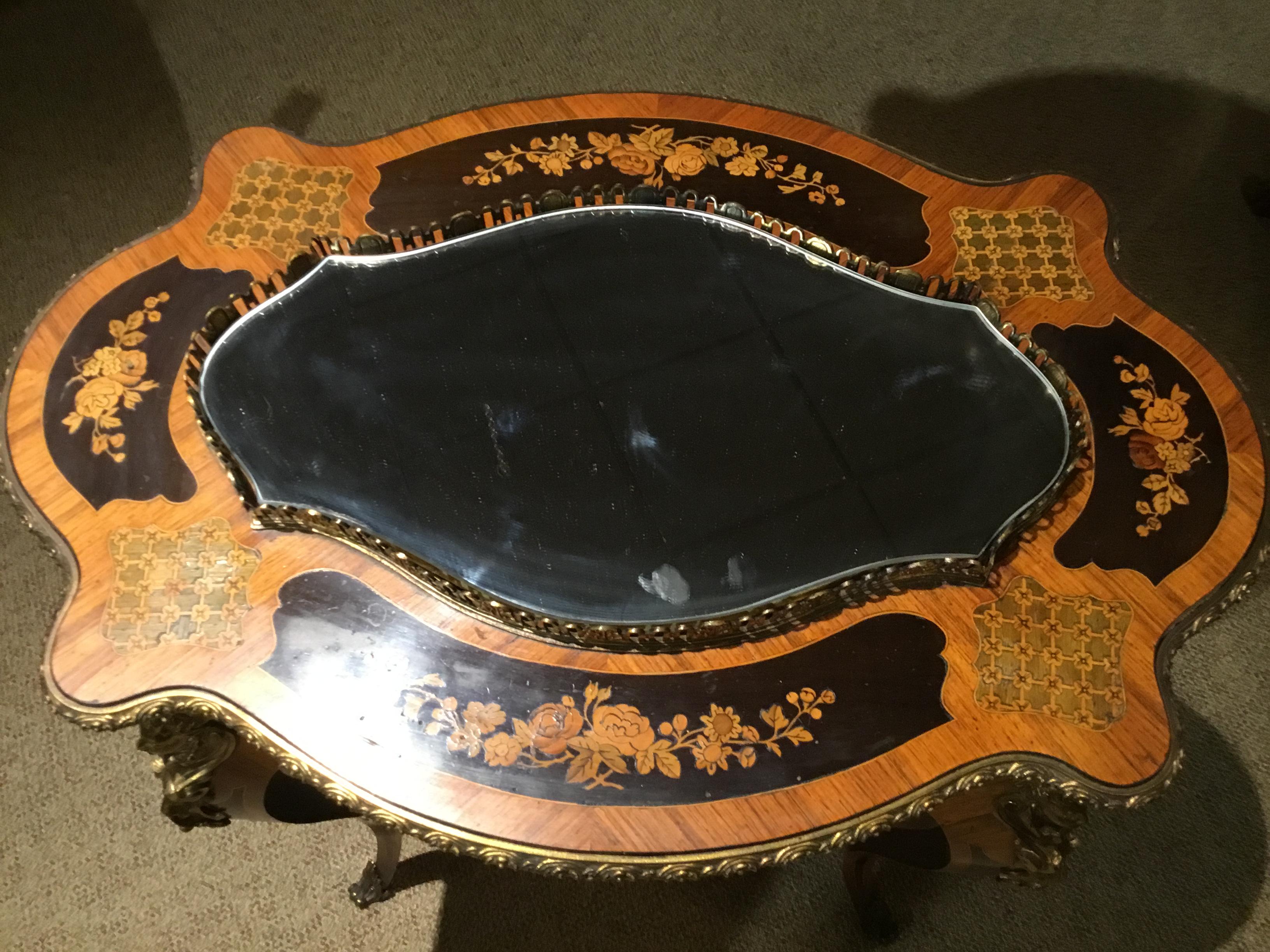 Marquetry of kingwood, satin wood, olive wood and ebony combined
To make an exceptional table. Foliate designs are centered on all
Four sides of this piece. The top is mirrored and has reticulated gallery.
Graceful oval shape and curved leg make