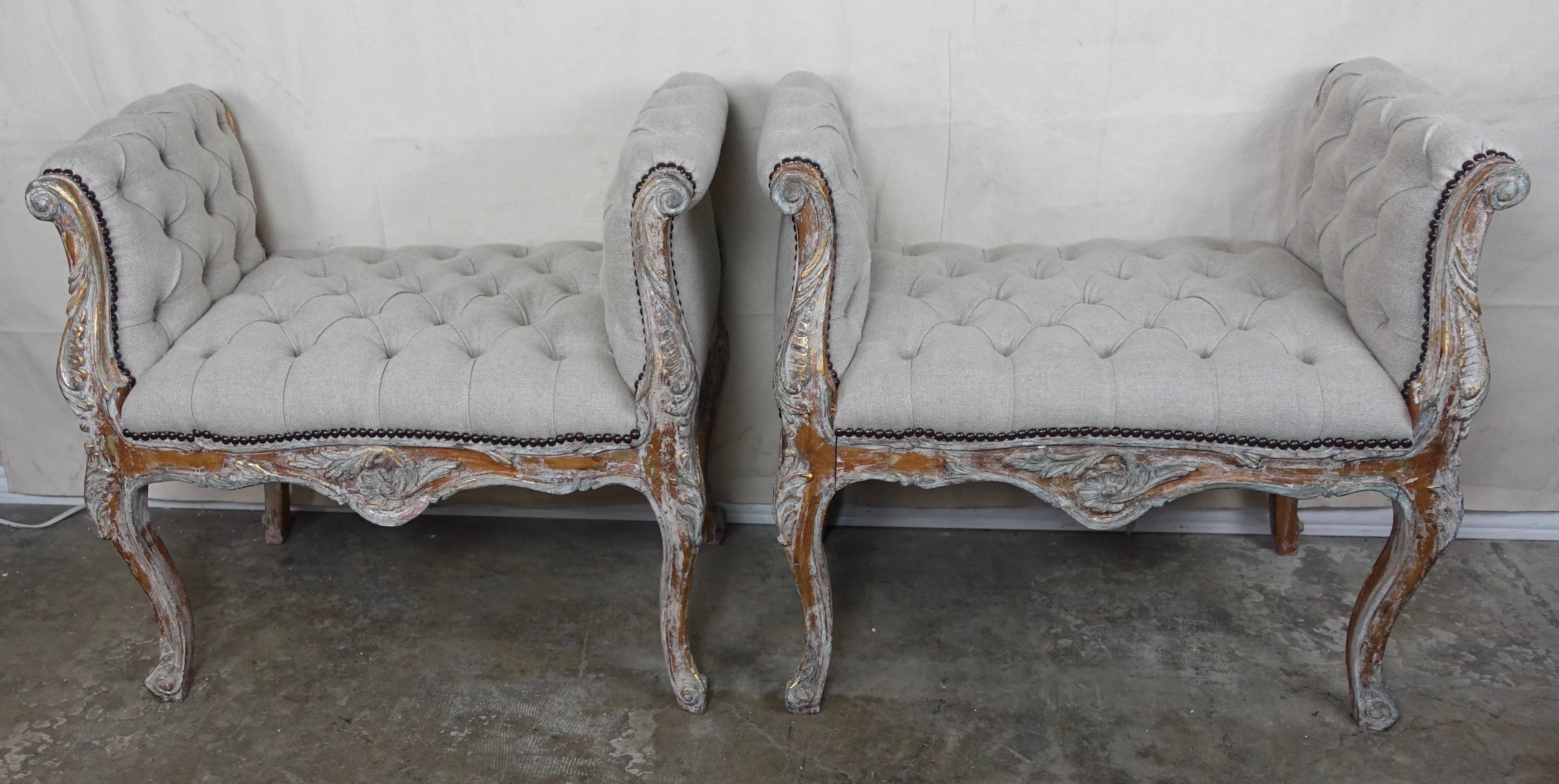 Pair of French Louis XV style benches in a painted and parcel-gilt worn finish. The benches are newly upholstered in oatmeal colored tufted Belgium linen with nailhead trim detail.