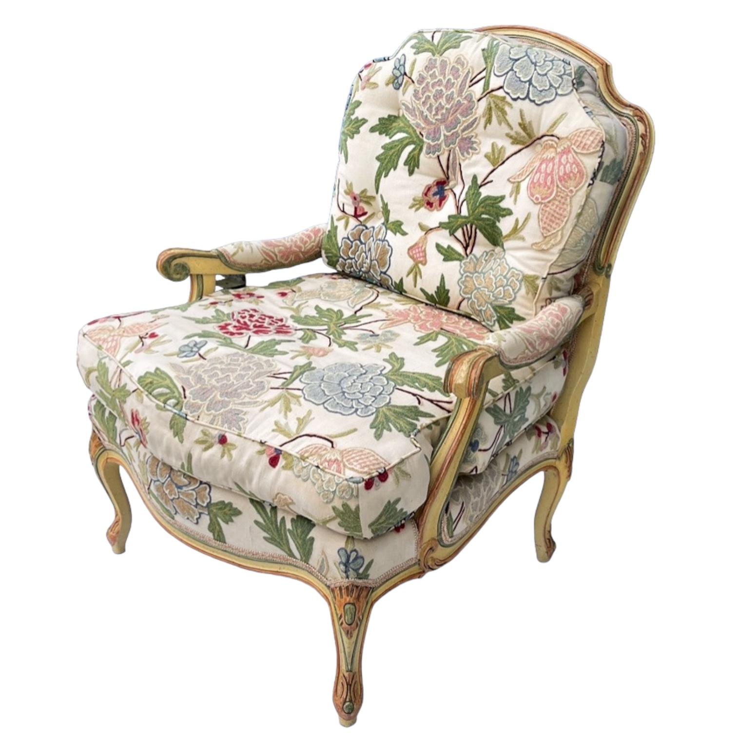 This is a pretty French Louis XV style bergere chair upholstered in a floral crewel. The frame is painted ivory, rose, and celadon. It is unmarked and most likely dates to the 1980s.