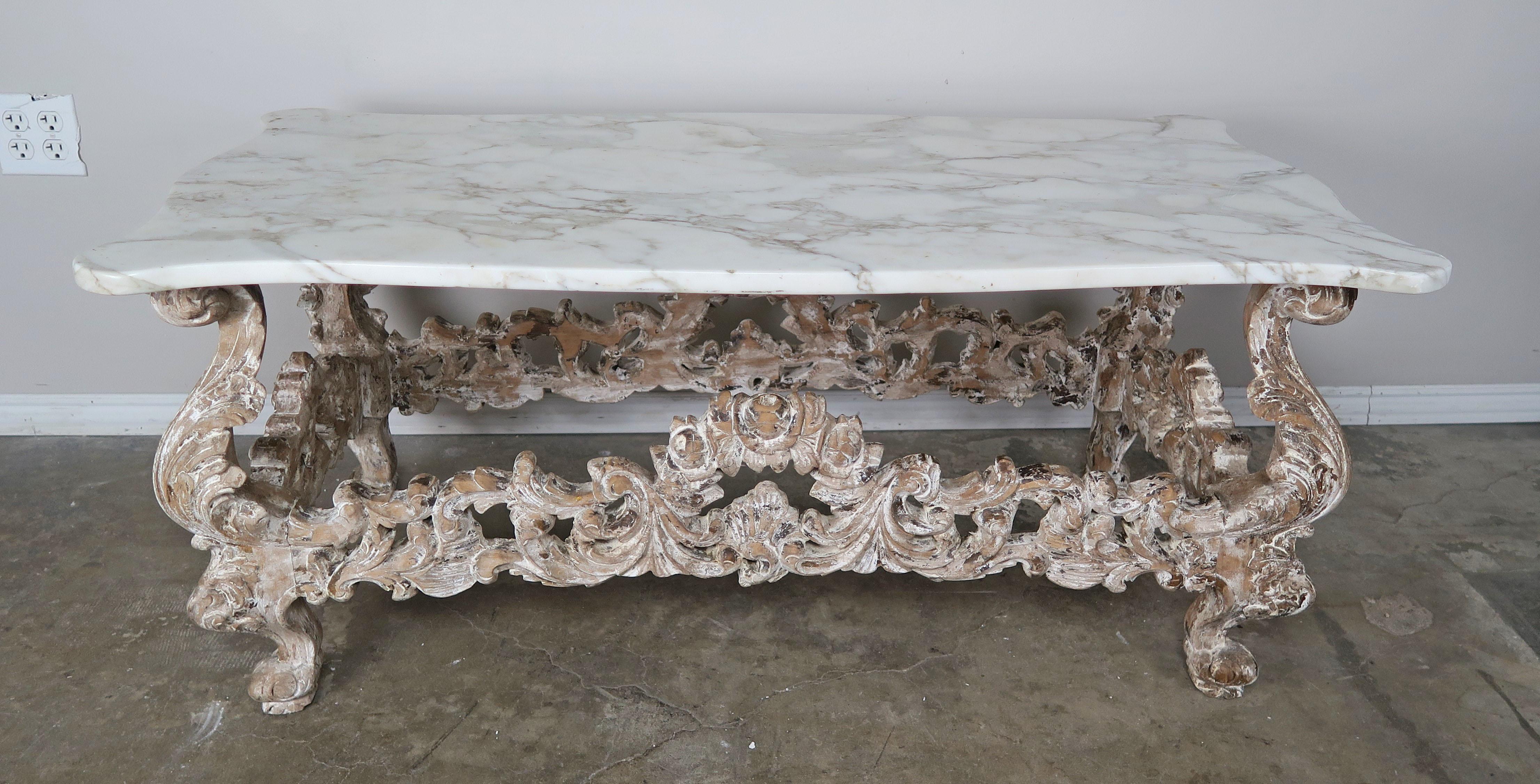 French Rococo style heavily carved and painted coffee table depicting swirling acanthus leaves throughout. The table stand on four cabriole legs with rams head feet. A beautiful serpentine shaped Carrara marble top sits on this exquisite base. Worn