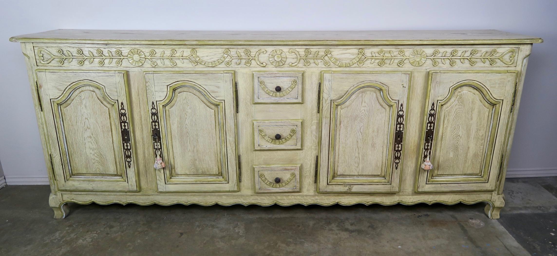 French Louis XV style carved elm painted buffet with a beautiful worn finish. The sideboard stands on four legs, cabriole shaped connected by a scalloped bottom edge detail. There are four doors with original antique hardware that flank three