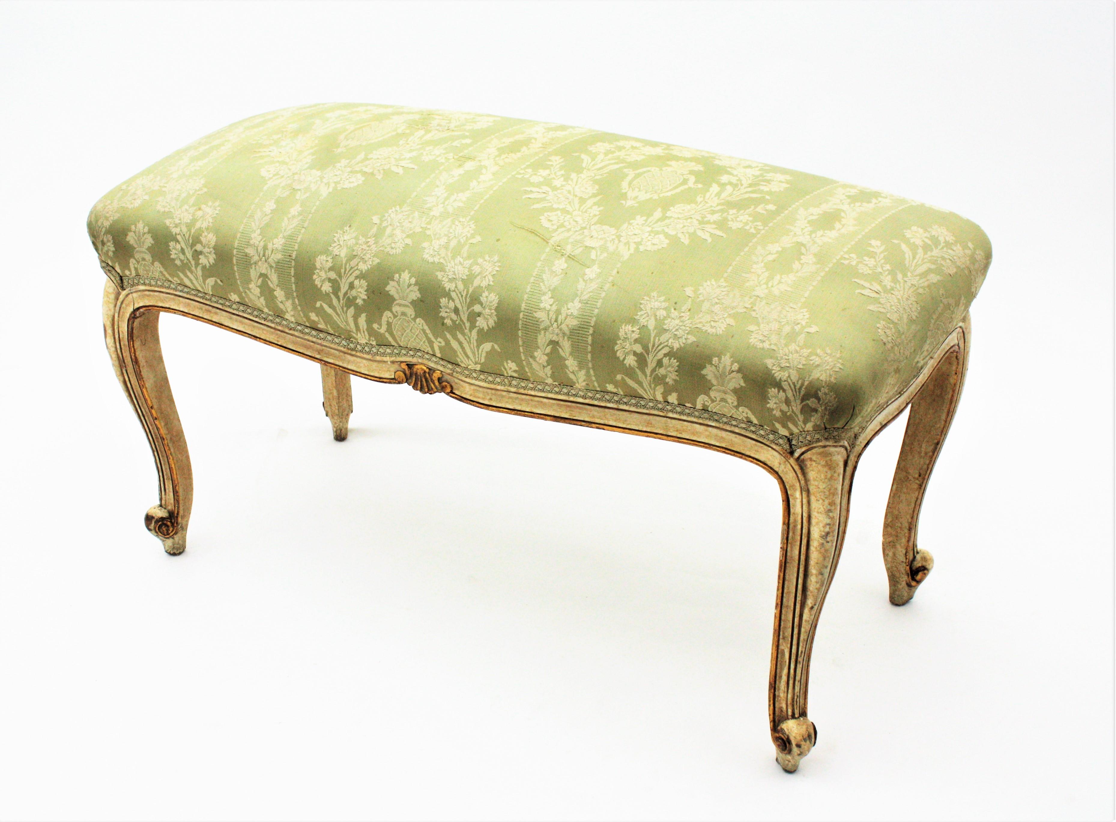 Stylish 19th Century Louis XV style carved wood bench patinated in ivory color with gold leaf gilt accents. France, circa 1850.
This bench or stool is raised on four cabriole shaped legs with carved scroll motifs and it is accented by decorative