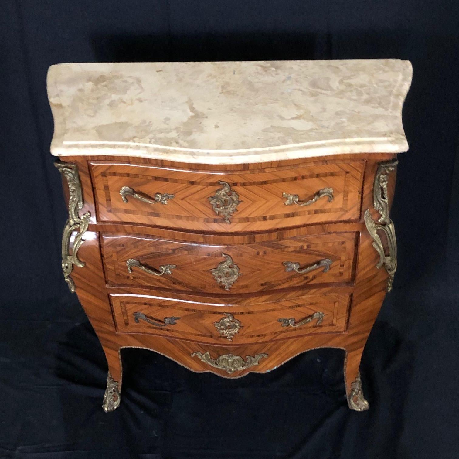 Petite Louis XV style marble top chest or commode having beautiful banded herringbone marquetry serpentine shaped front with three drawers and decorative gold bronze mounts. The lovely cream and ivory Italian marble has corners beveled with curves