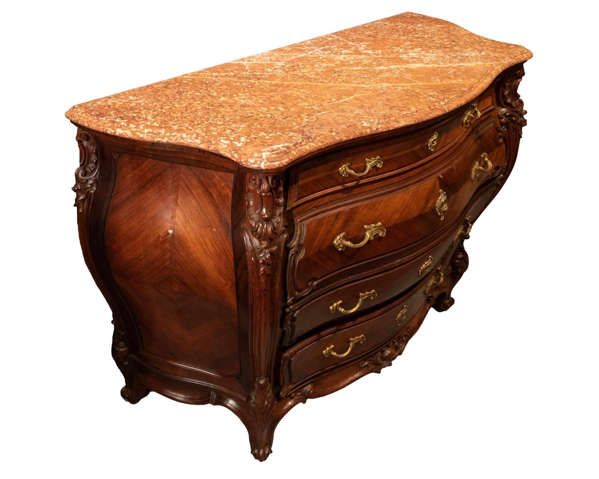 French Louis XV style rosewood Bombé commode with marble top. A Louis XV style commode in carved and book-matched veneer rosewood, four drawers each with two handles and a lock escutcheon in gilt bronze, with a marble top. French, late 19th