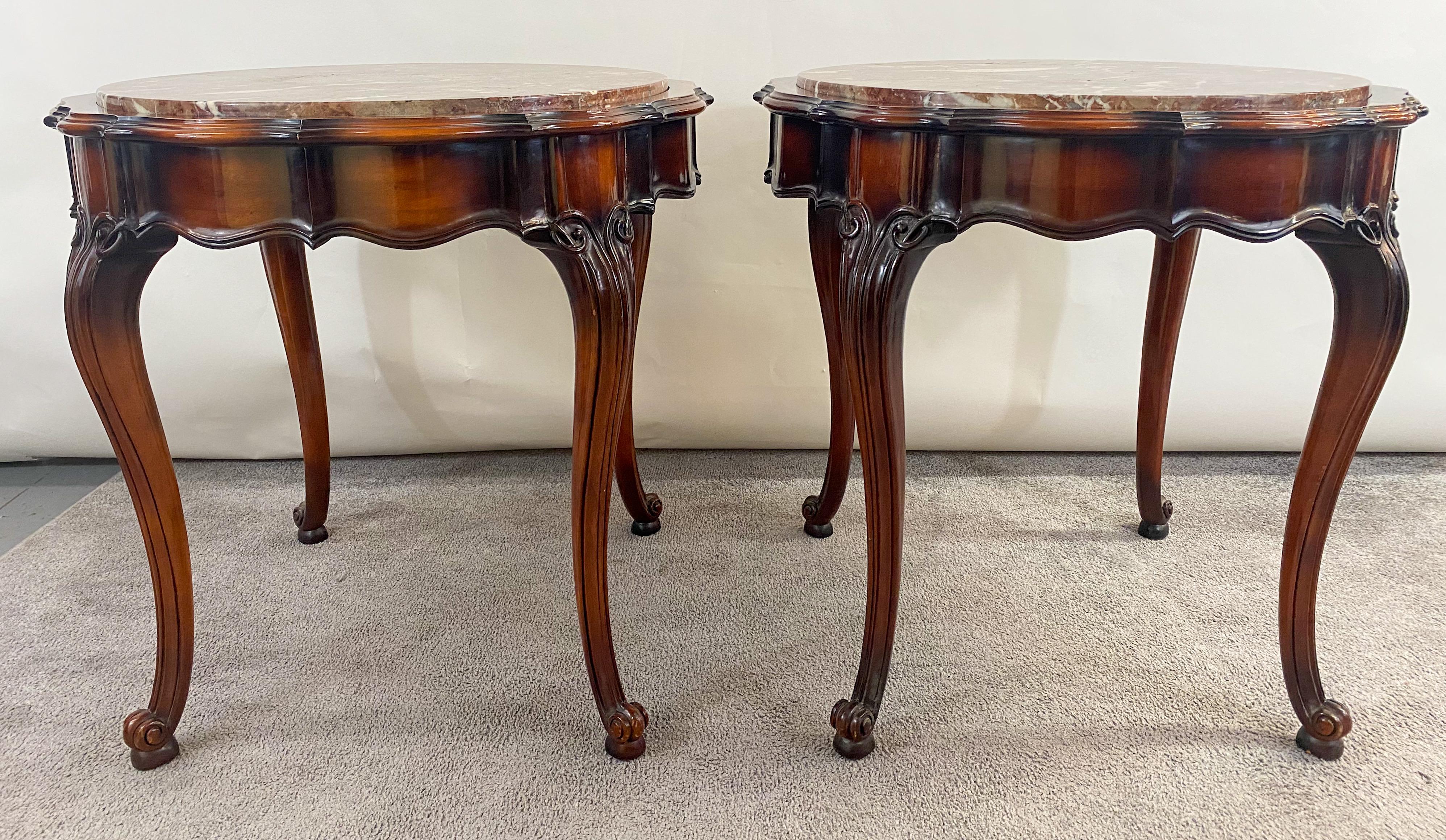 An elegant pair of French Louis XV style Mahogany side or end tables. The round shaped tables have a marble top showing beautiful grains in cherry tone color. The tables are finely carved and feature Cabriole legs. The pair of French Louis XV style