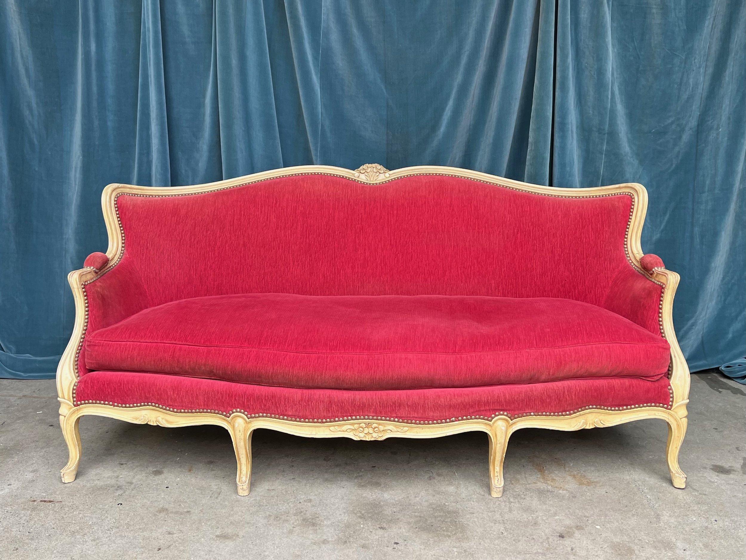 Ein atemberaubendes französisches Sofa im Louis-XV-Stil aus den 1920er Jahren, gepolstert mit reichem rotem Samt und einem cremefarbenen Holzrahmen. Die Messingnageldetails verleihen einen zusätzlichen Hauch von Eleganz und Raffinesse. Das Sofa ist