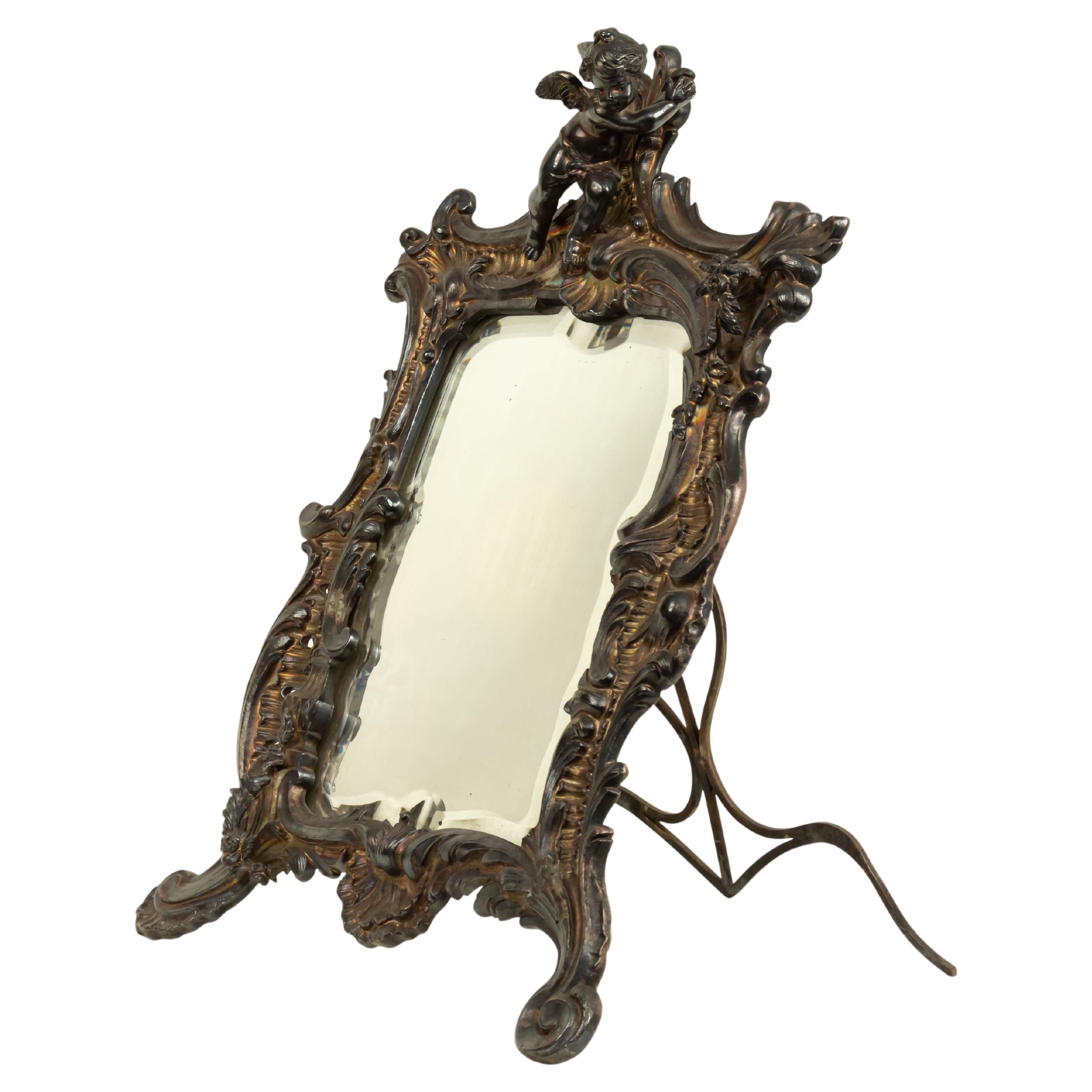 Specchio da toeletta rettangolare in argento in stile Luigi XV (XIX secolo) con disegno a volute e cupido nella parte superiore.
 