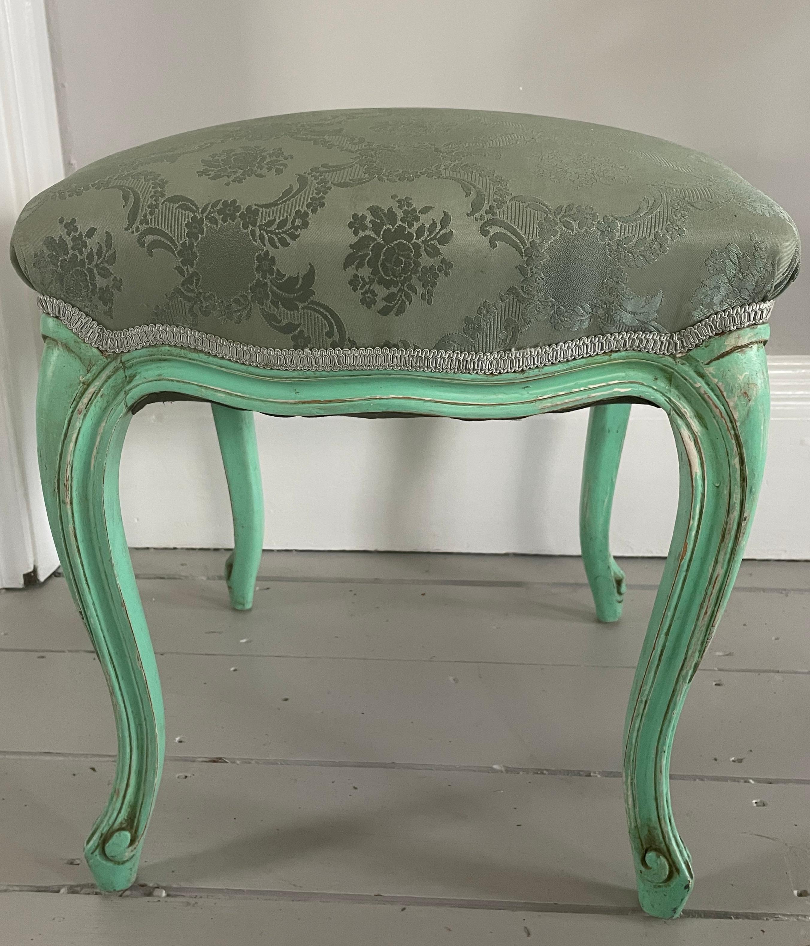 This is a lovely and graceful wooden (quite possibly walnut) stool, made in the style of Louis XV, and painted in a distinctive minty green. The cushy damask upholstery is in very good condition and the whole in untouched and very good original