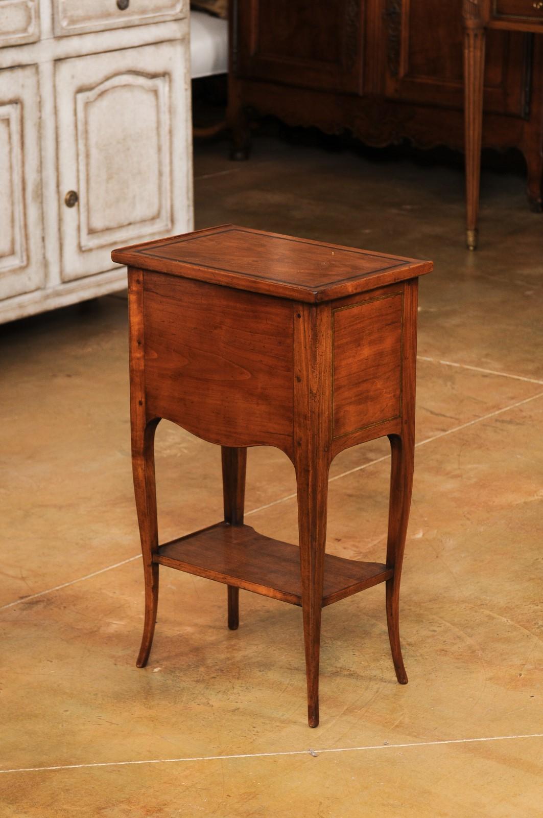 A French Louis XV style cherry wood table-chiffonnière from the 20th century with three small drawers and lower shelf. Created in France during the 20th century, this cherry wood side table, called a table-chiffonnière in French, was designed to be