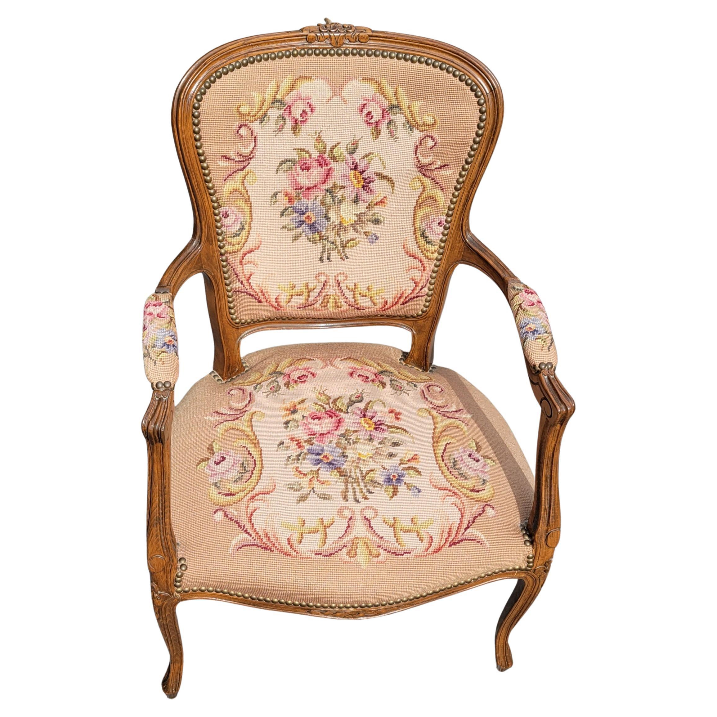 French walnut needlework armchair in the Louis XV style and carved with a floral crest. The needlework seat and back are bordered with brass studs. Measures 23