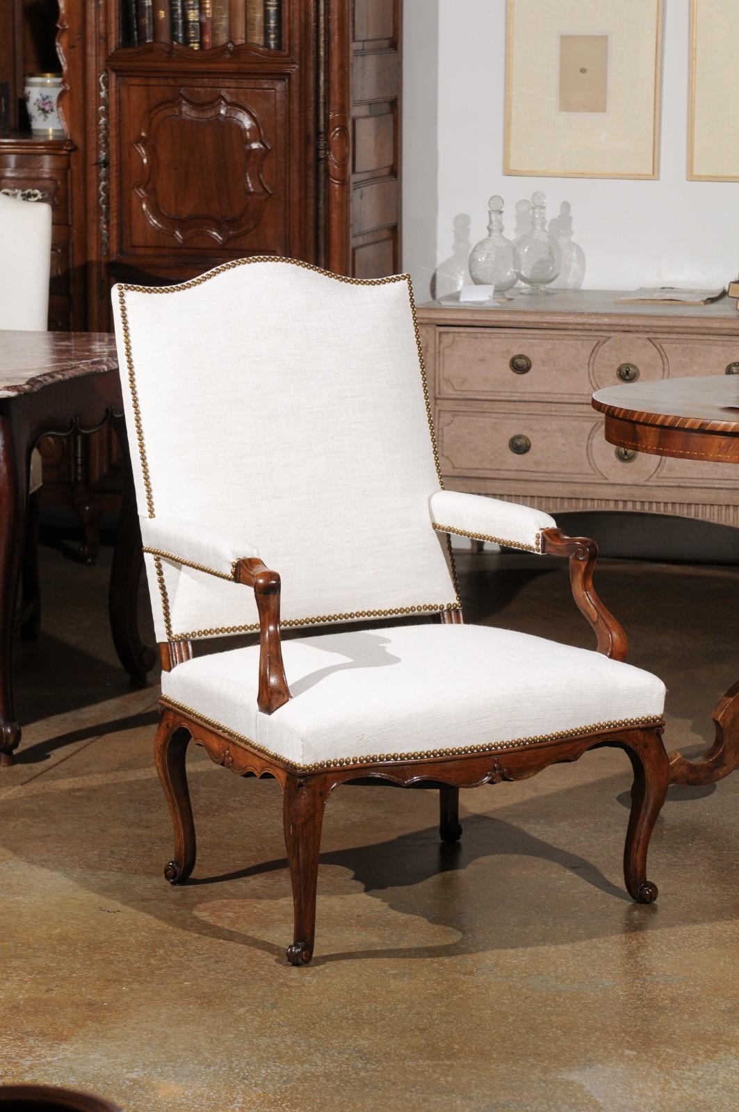 A French Louis XV style walnut armchair from the 19th century, with linen upholstery and antique brass nailhead trim. Born in France during the 19th century, this exquisite fauteuil features the stylistic characteristics of the Louis XV era. The