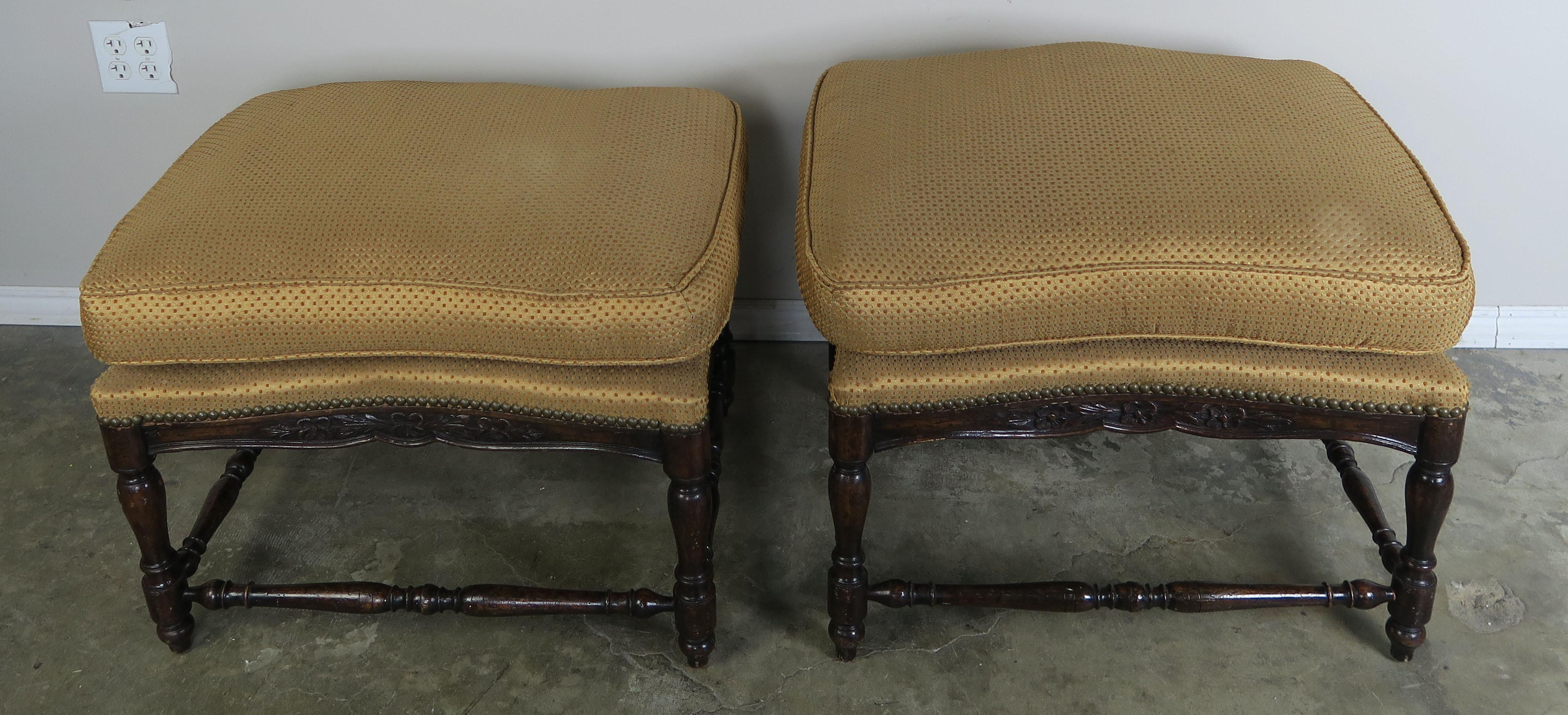 Pair of French Provincial style walnut benches that are upholstered in a high end golden colored designer silk with gold chenille flecks throughout and detailed with antique brass colored nailhead trim. The cushions have feather and down inserts.