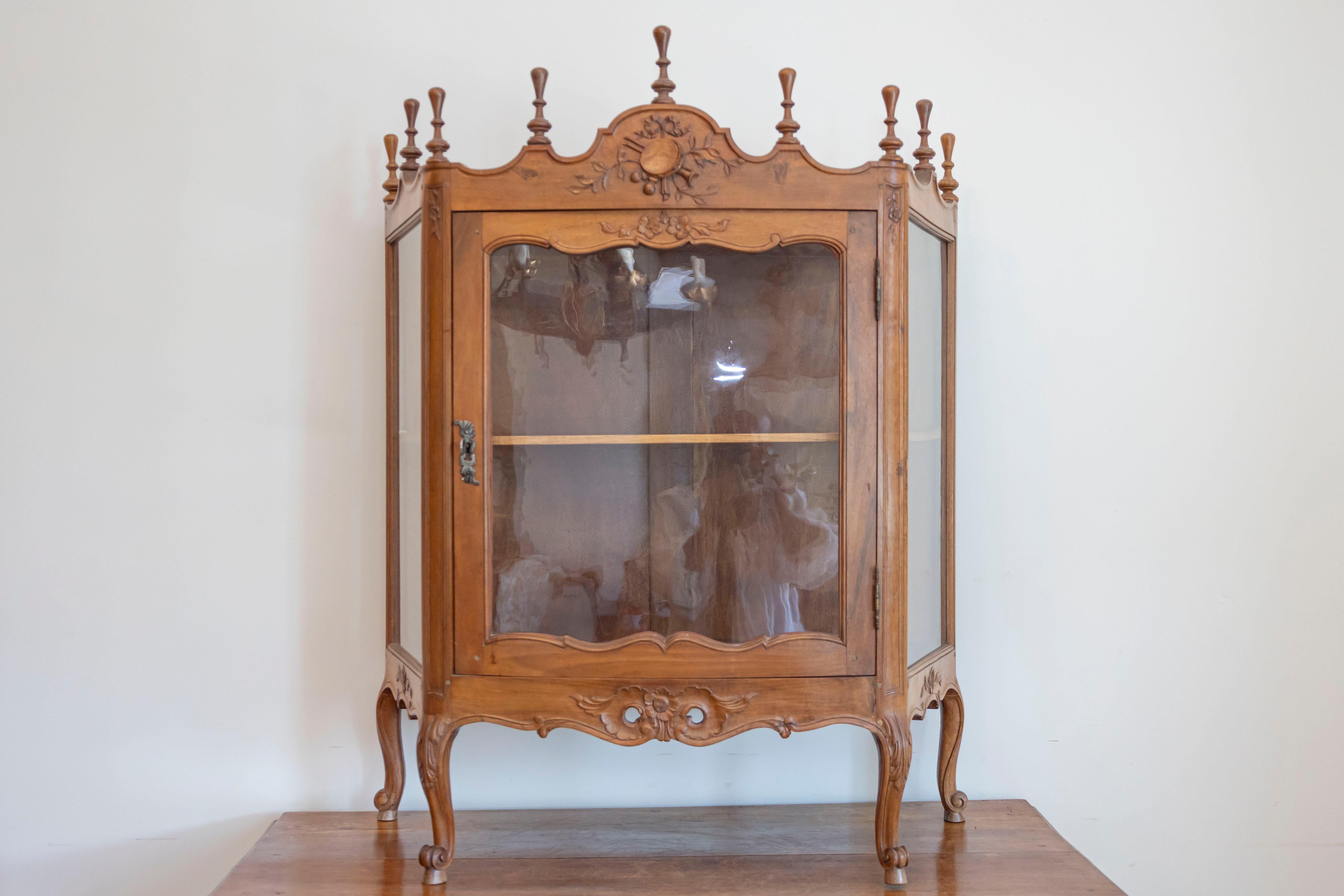 A French Louis XV style walnut display cabinet from the 19th century, with glass door, carved motifs and petite finials. Created in France during the 19th century, this Louis XV style petite vitrine captures our attention with its rhythmic