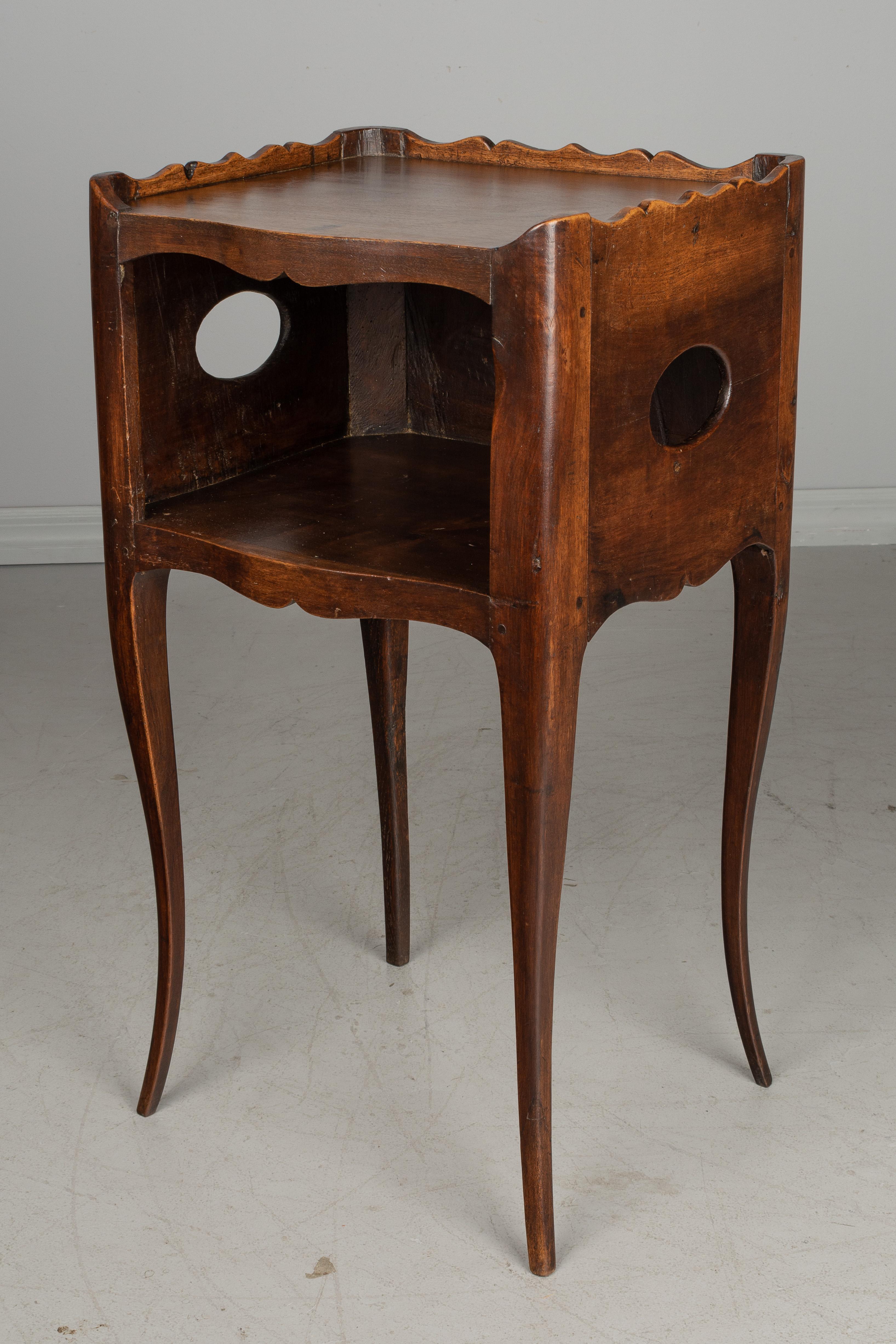 A Louis XV style country French side table or nightstand made of solid walnut, with open niche and pierced cut-out oval shapes on the sides. Scalloped apron and gallery surrounding the top. Curved corners and slender legs waxed finish. All original.