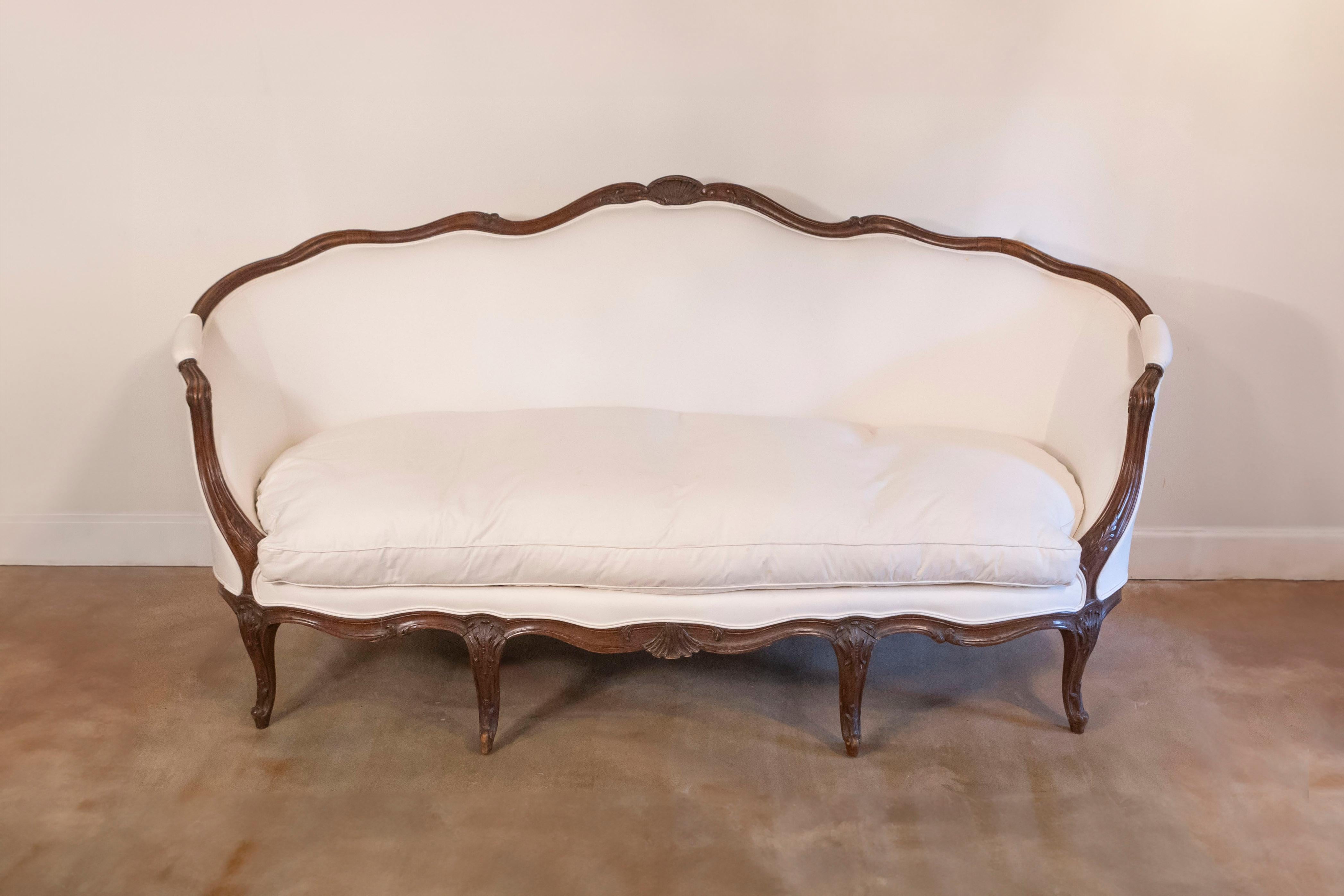 Canapè francese in noce in stile Luigi XV della metà del XIX secolo, con schienale avvolgente, braccioli a voluta, gambe cabriole e tappezzeria beige nuova. Questo canapè francese presenta un delicato schienale avvolgente, ornato da una cresta