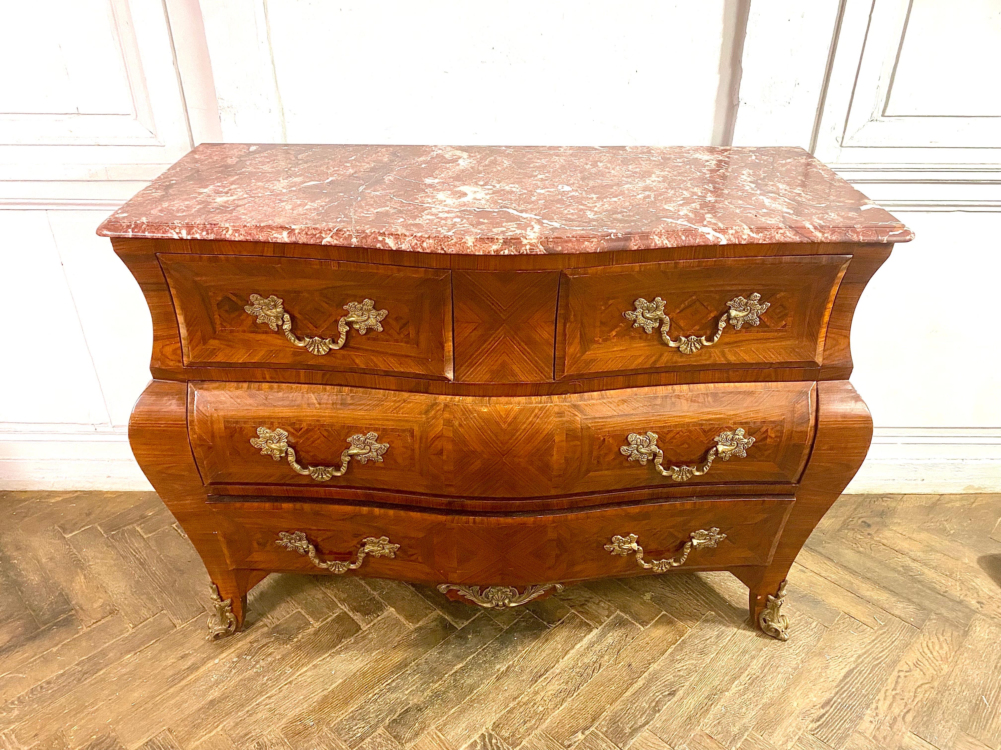 Bellissima cassettiera a tomba in stile Luigi 15 che si apre con quattro cassetti. Questo elegante mobile in legno nativo intarsiato con un motivo geometrico e puntiforme presenta ornamenti in bronzo come le maniglie dei cassetti e le scarpe