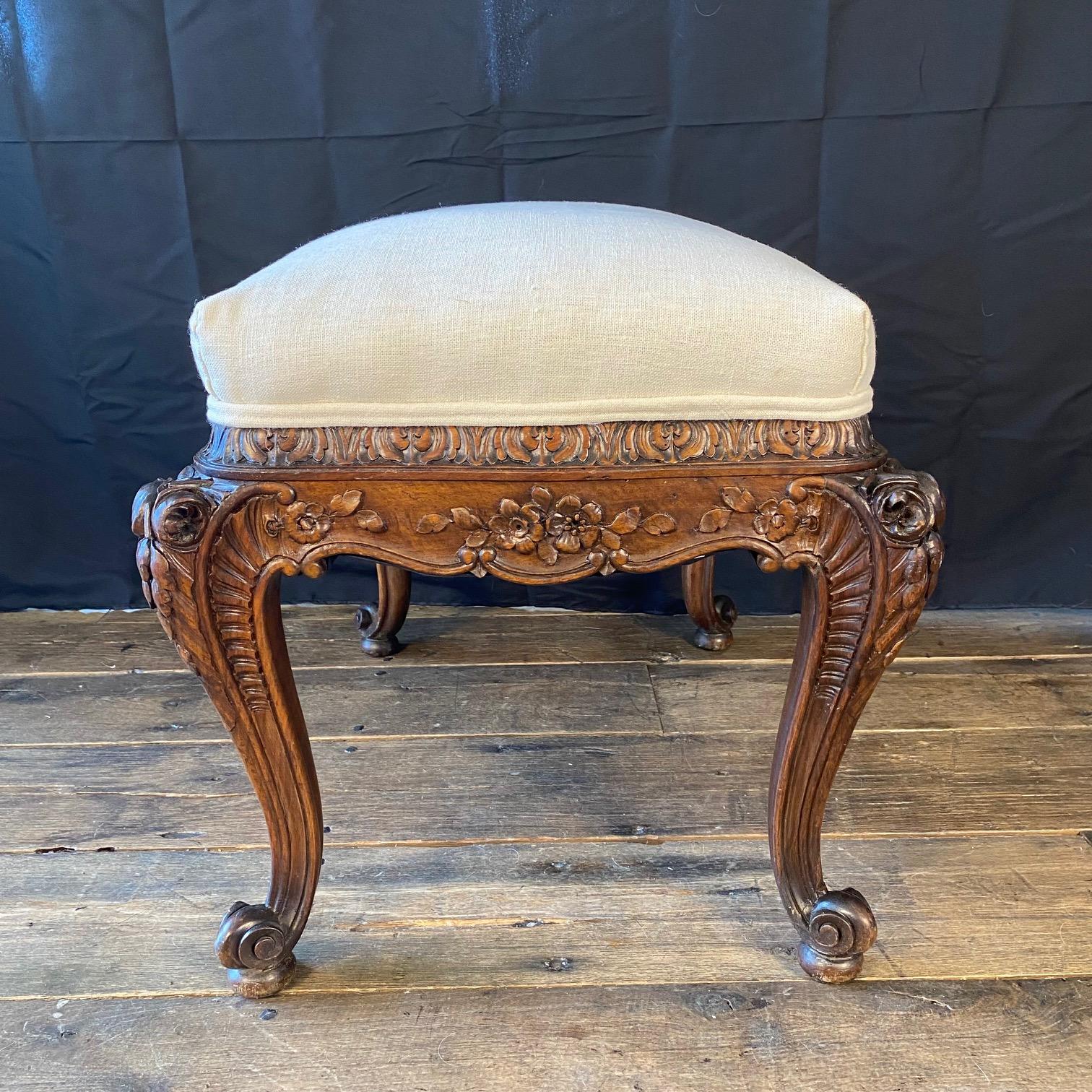 Exquisite carving on this French walnut bench or ottoman, embodying the graceful elegance of the Louis XV style. Built from solid walnut, the frame features a gently curved silhouette with detailed carved floral and foliate motifs adorning all four