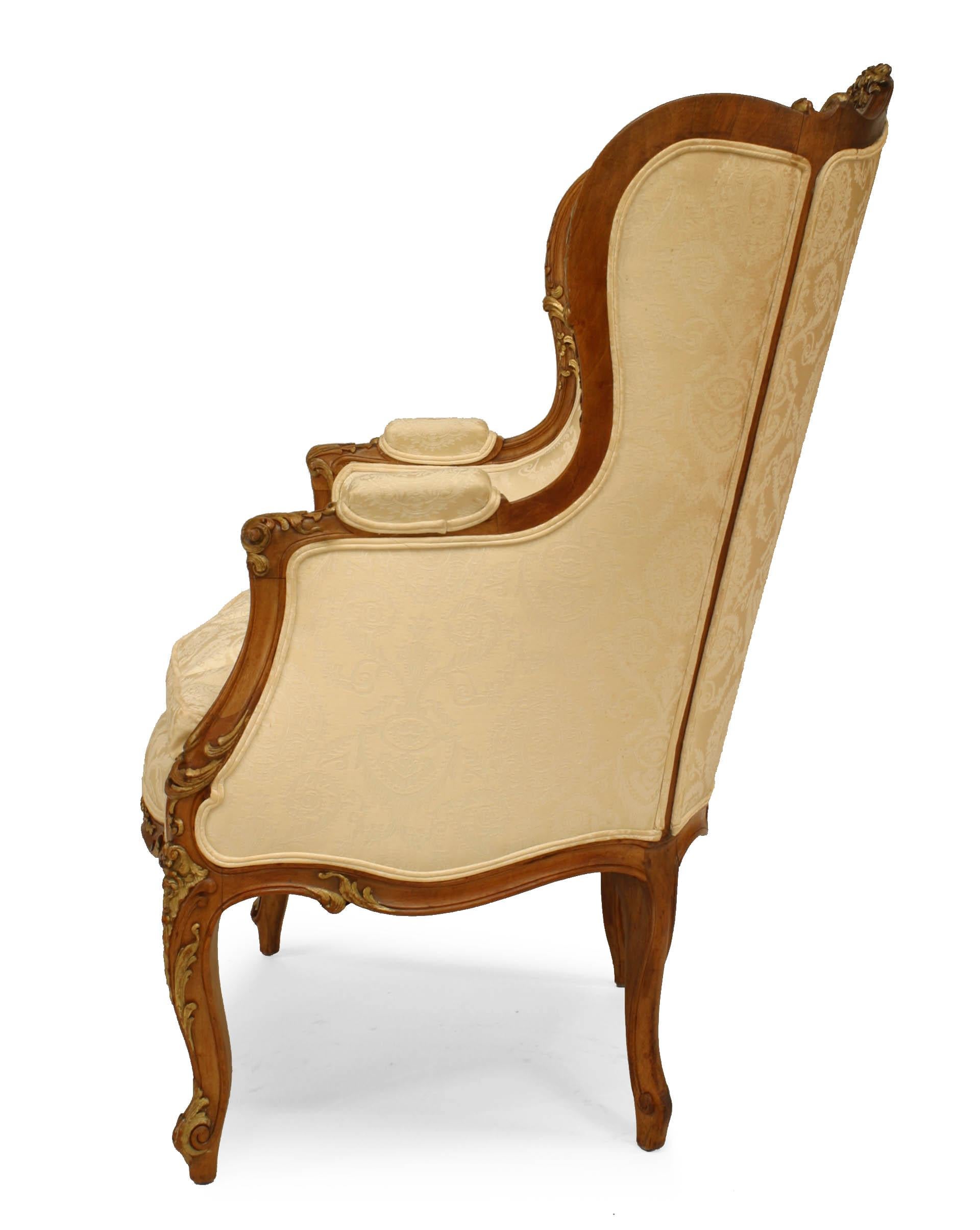 Late 19th early 20th century French Louis XV style walnut bergere arm chair with gilt trim, white upholstery, and wing back.