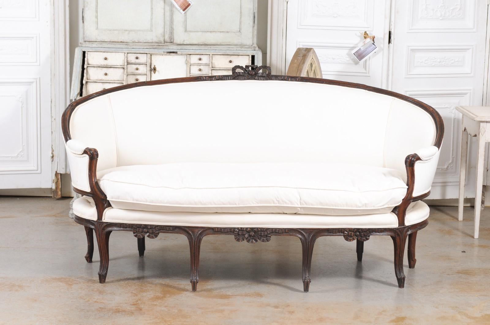 A French Louis XV walnut canapé en corbeille from the late 18th century, with carved bow and new upholstery. Created in France during the last decade of the 18th century, this canapé en corbeille reflects the delicate transition that happened