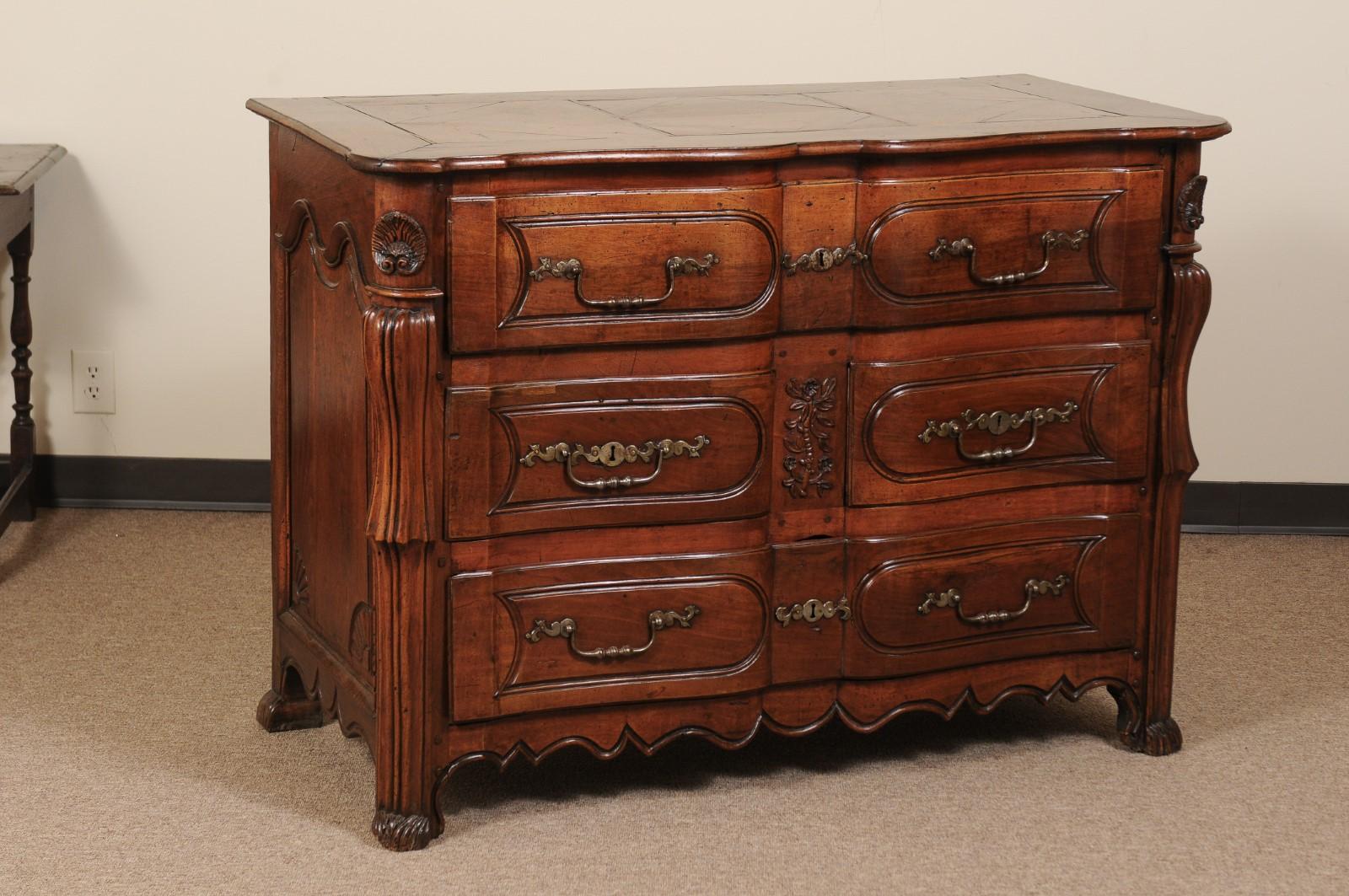 The Louis XV walnut commode with serpentine front, 3 paneled drawers with wrought iron hardware, caved sides with shell detail and shaped apron below. 

 