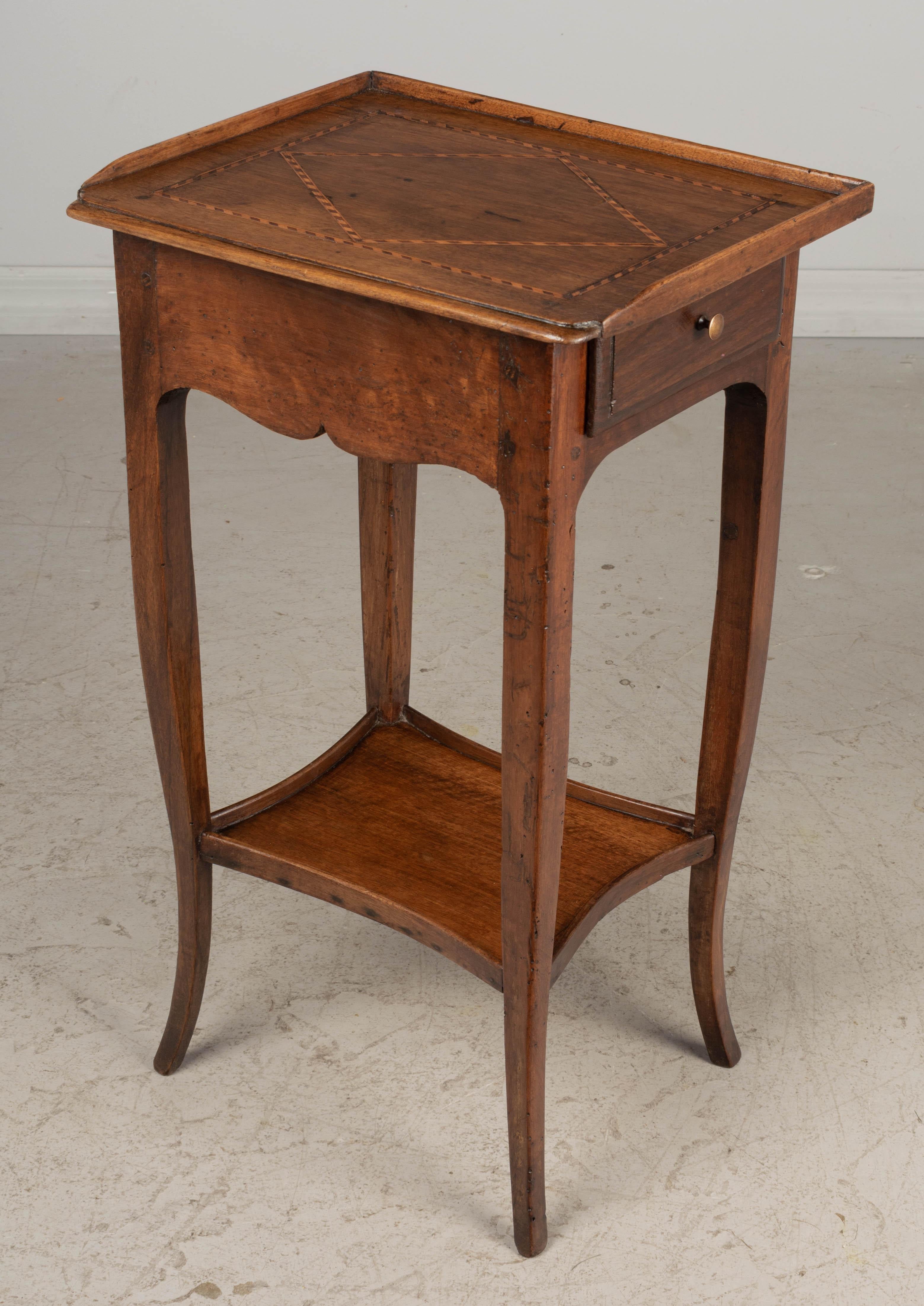 A French Louis XV style writing or side table made of solid walnut. Single dovetailed drawer on the right side. Top has marquetry inlaid detail and curved front corners with wood trim gallery on three sides. Elegant curved legs and lower shelf. All