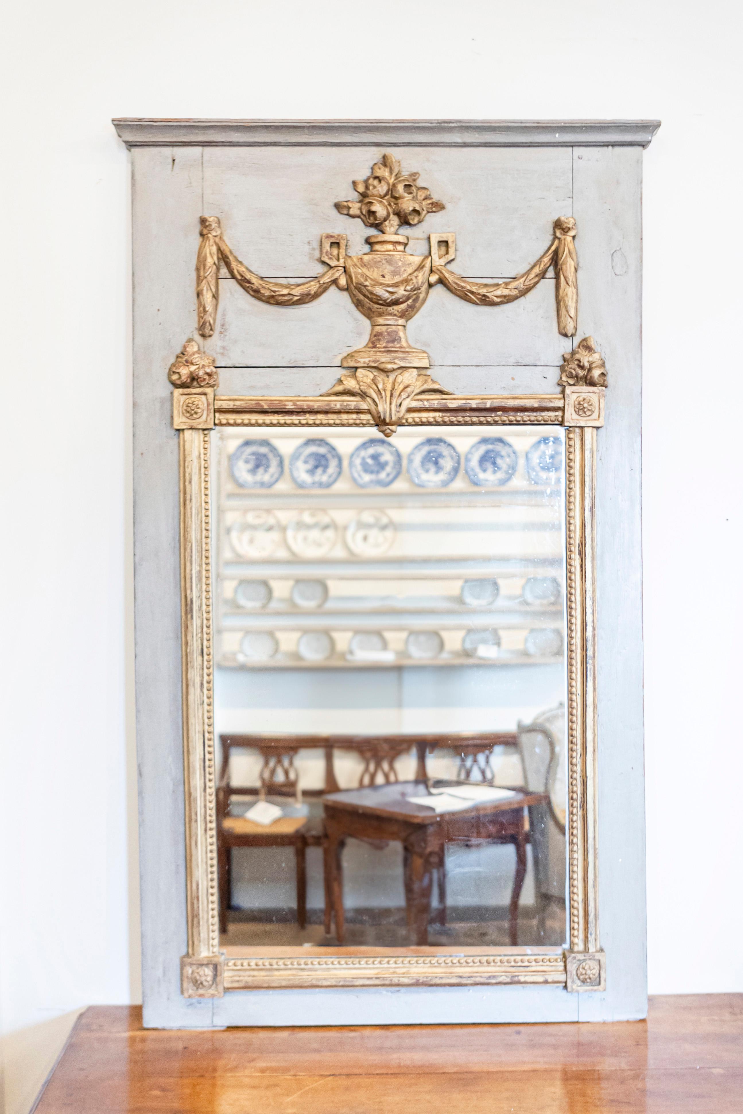 A French Louis XVI period painted trumeau mirror from circa 1790 with carved giltwood bouquet of roses in vase surrounded by swags. This exquisite French Louis XVI period trumeau mirror, dating back to circa 1790, epitomizes the elegance and refined