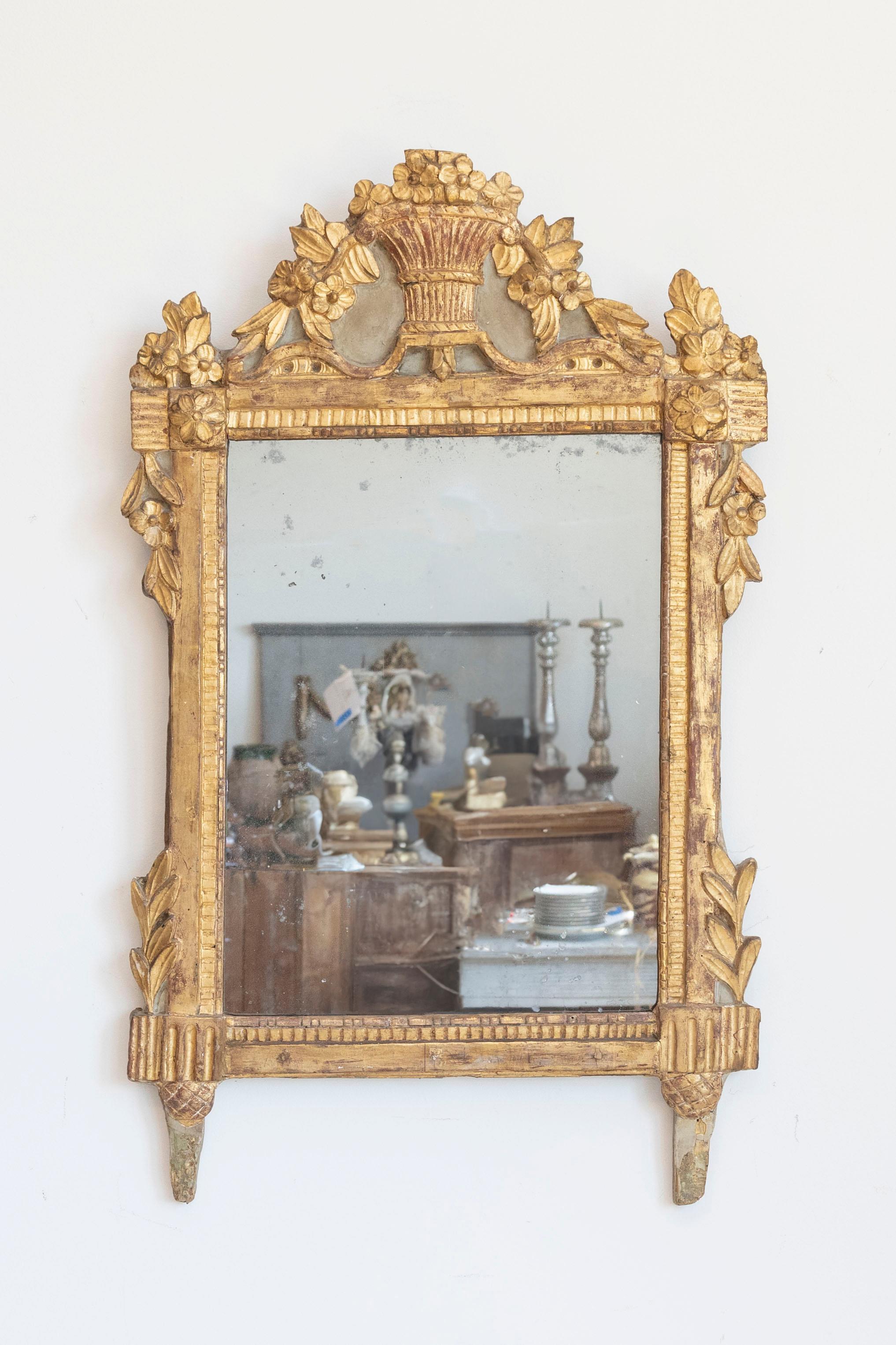 A French Louis XVI period giltwood mirror from the 18th century with carved crest depicting a bouquet of flowers falling from a wicker basket, carved foliage and old mirror plate. This stunning French Louis XVI period giltwood mirror from the 18th