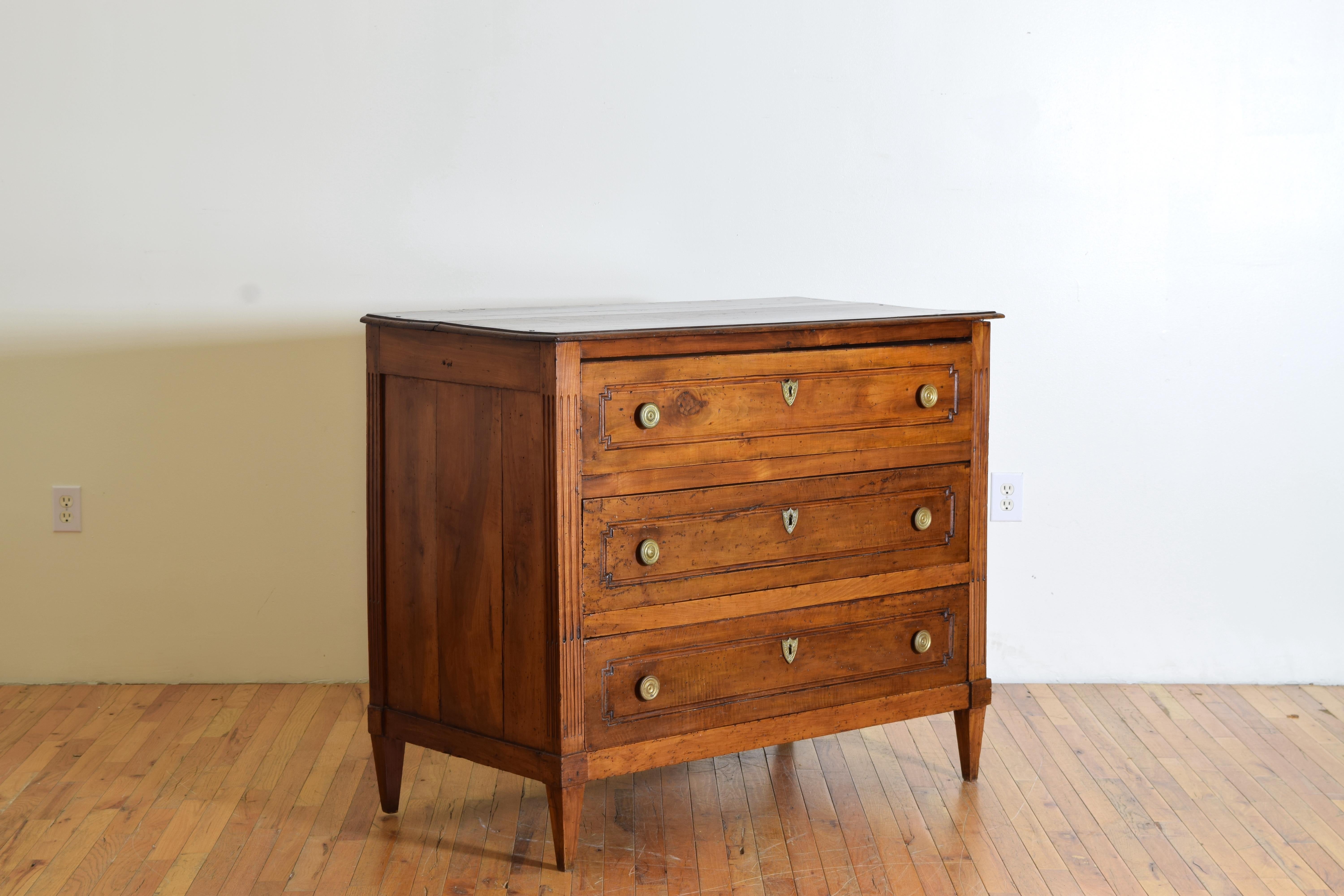 Having a two board rectangular top above a conforming case with fluted corners front and back, the three drawers with carved panels, circular brass pulls and brass escutcheons, raised on square tapering legs