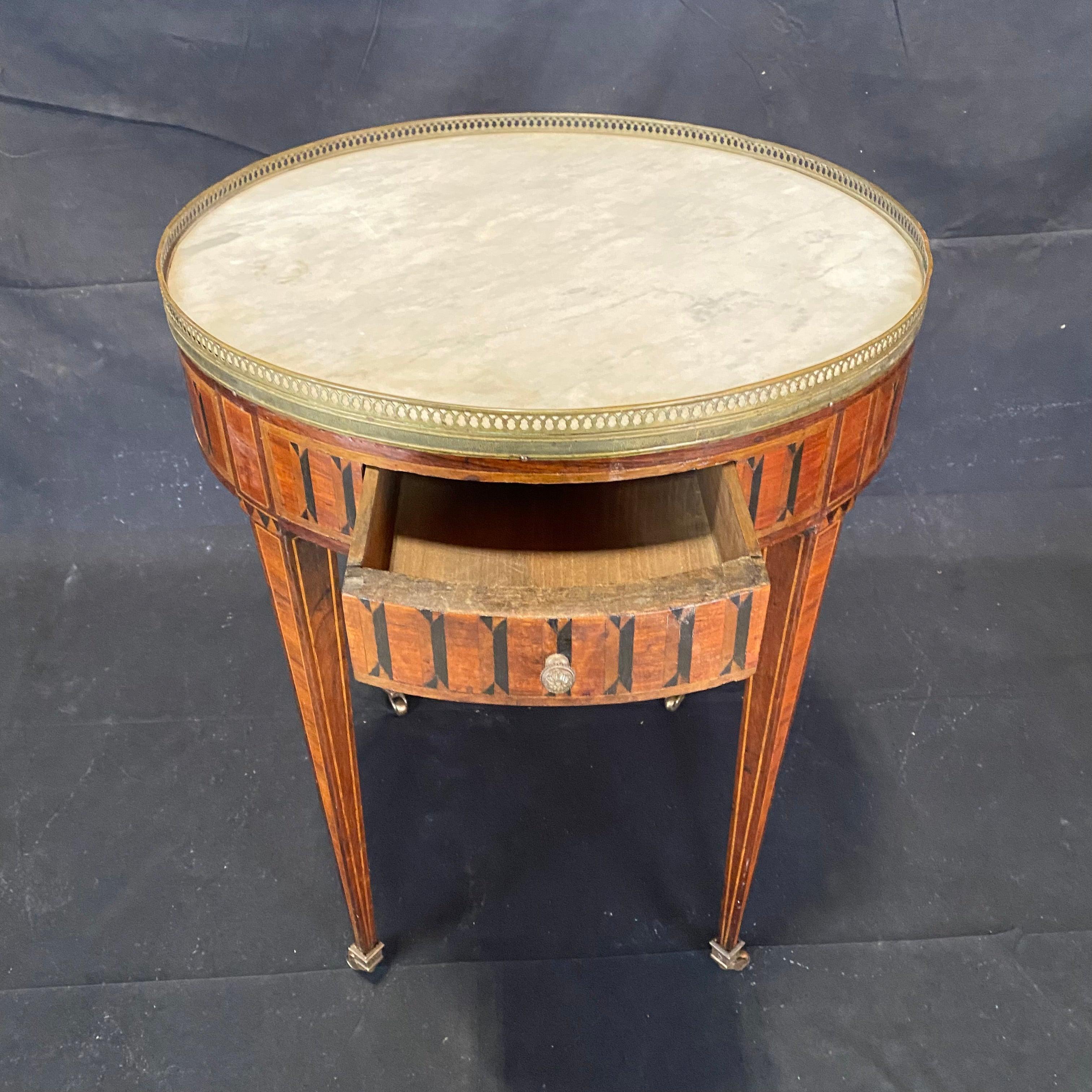 Louis XVI style marble top bouillotte table with elaborate marquetry. Two drawers and pull out tirelles slides with red tooled leather. White Carrera marble top is surrounded by a pierced bronze gallery. Marble has small chip (see photos). The table