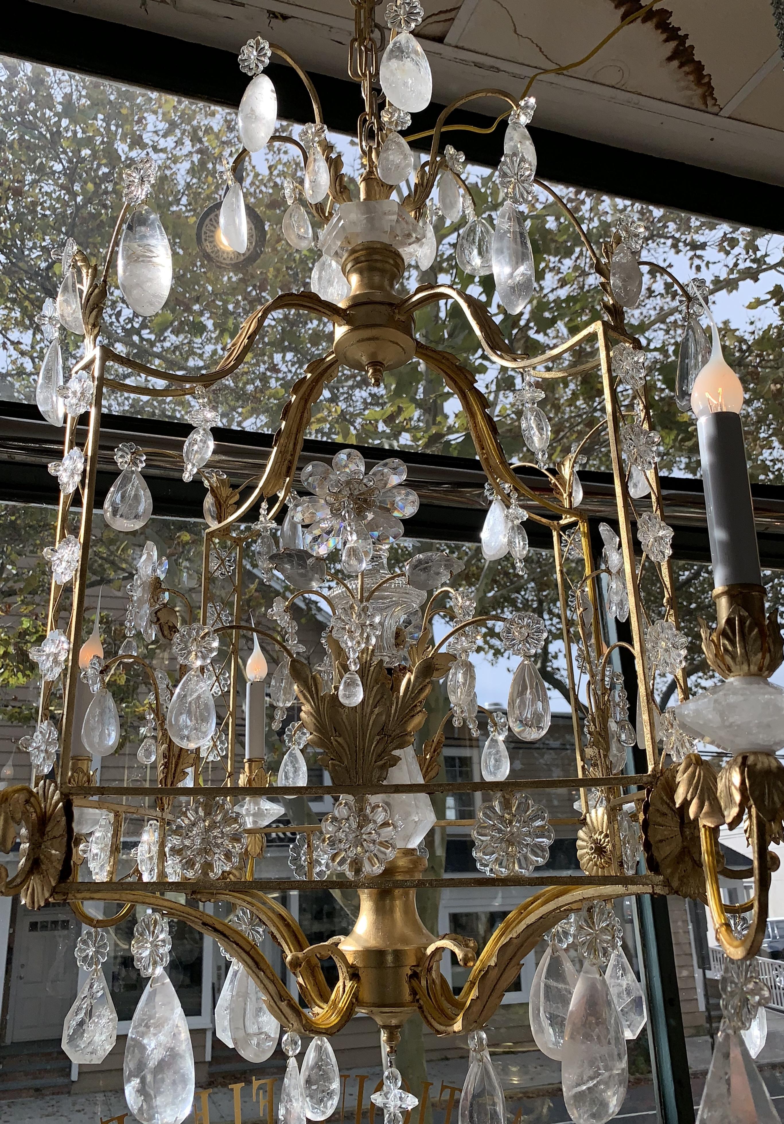 A wonderful French Louis XVI style Baguès style eight-light chandelier featuring rock crystal throughout on a gilt metal pagoda form with rock crystal rosettes framing the sides and rock crystal flowers in the center and gilt leaves accenting on the