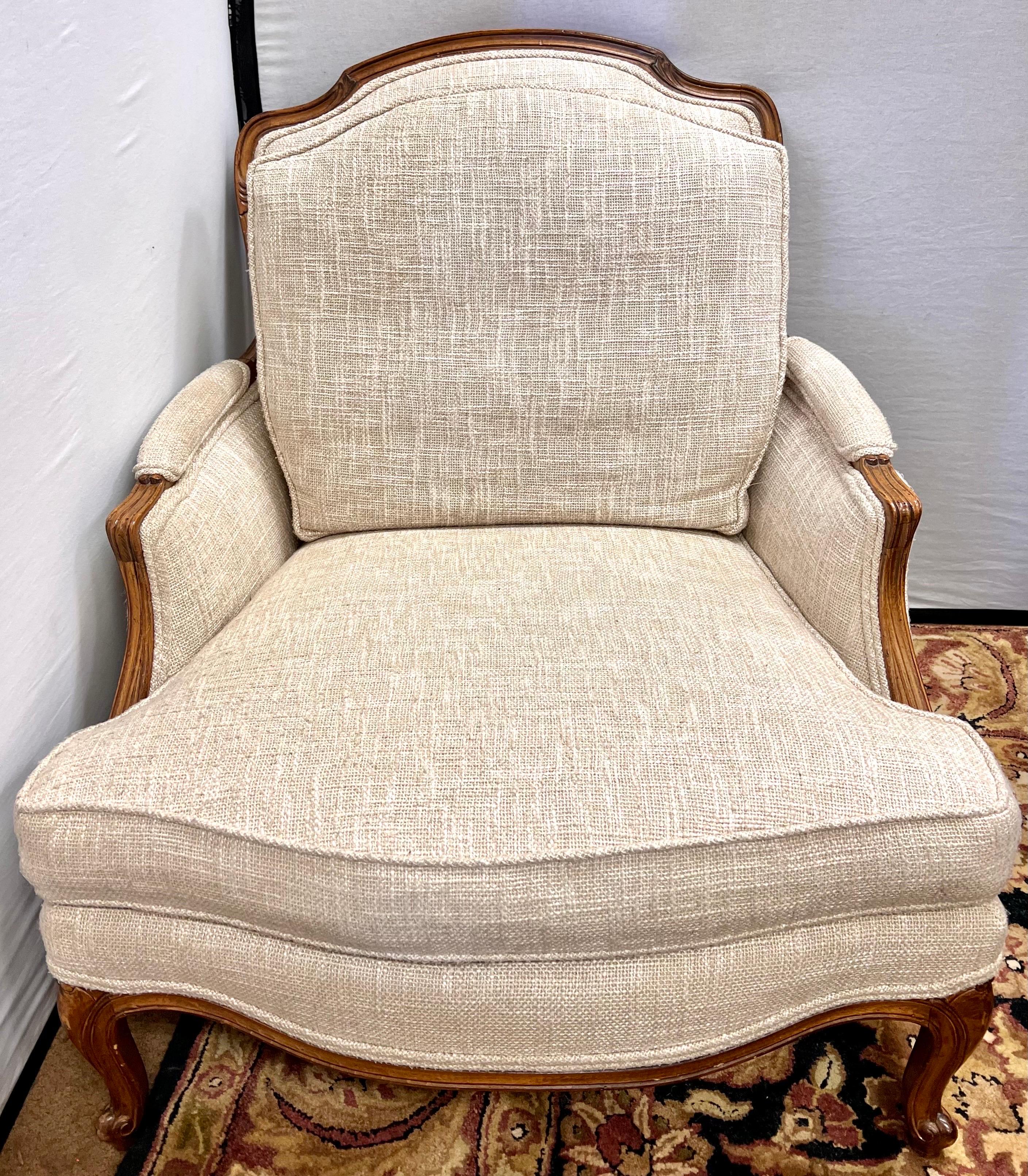 The generously proportioned Versailles bergere chair and ottoman are Louis XVI inspired with delightful handcarved detailing. Upholstered in a neutral beige linen fabric. Ottoman dimensions are 34