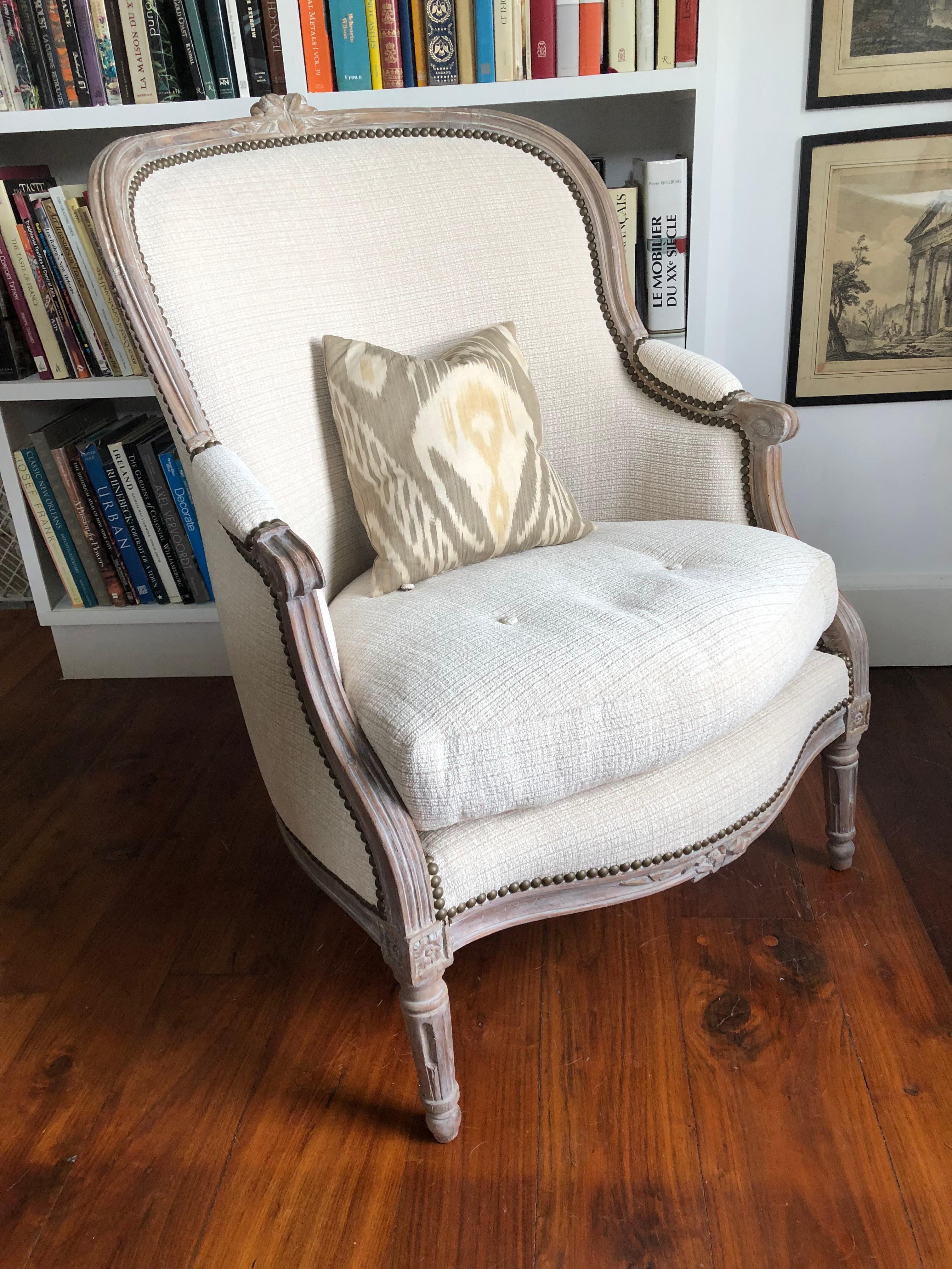 A French Louis XVI period bergère chair with a carved beechwood frame, bleached with a light whitewash, circa 1790. Recently re-upholstered in a cream cotton woven fabric with nailhead trim. Includes small back pillow in silk Ikat. Very sturdy and