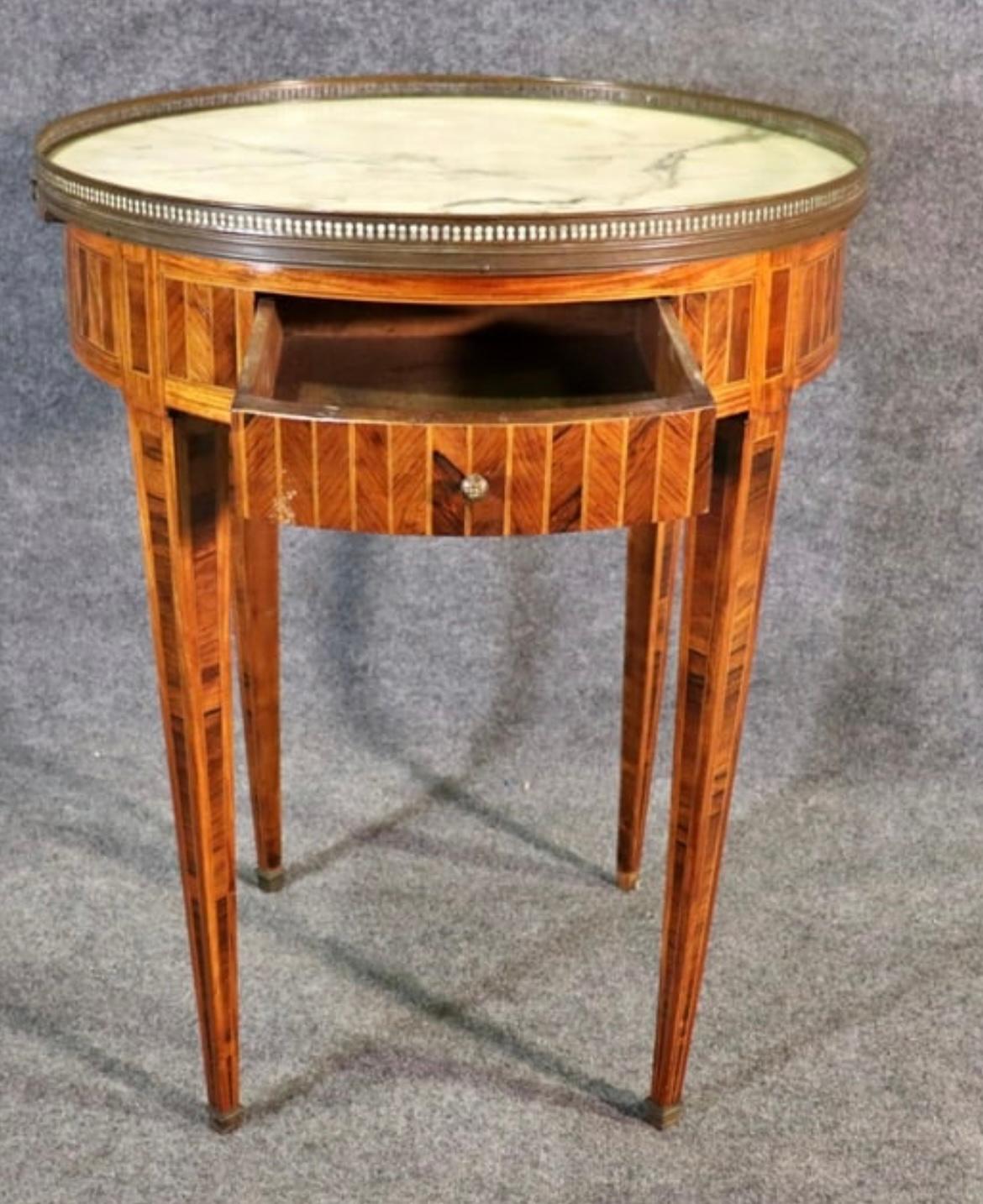 A French Louis XVI marble-top Bouillotte table in hardwood marquetry with a brass gallery and sabots, two small drawers and two pull-out leather covered tablets in the apron.  Circa 1800.  