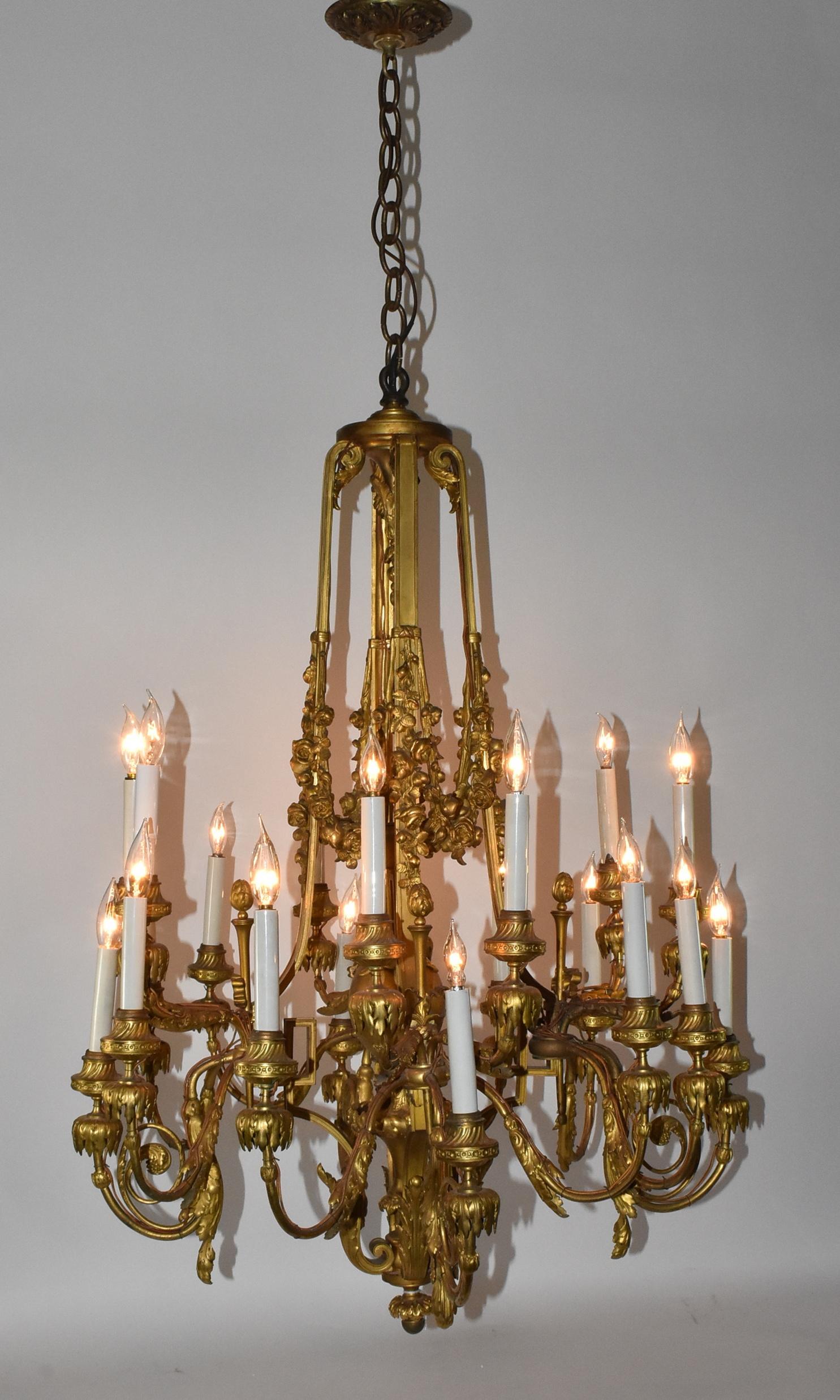 Patinated bronze ormolu twenty light chandelier. Converted from a candle fixture. Four scrolled arms with decorative torch detail. Center two handled urn surrounded by draped swags of roses. Dimensions: 52
